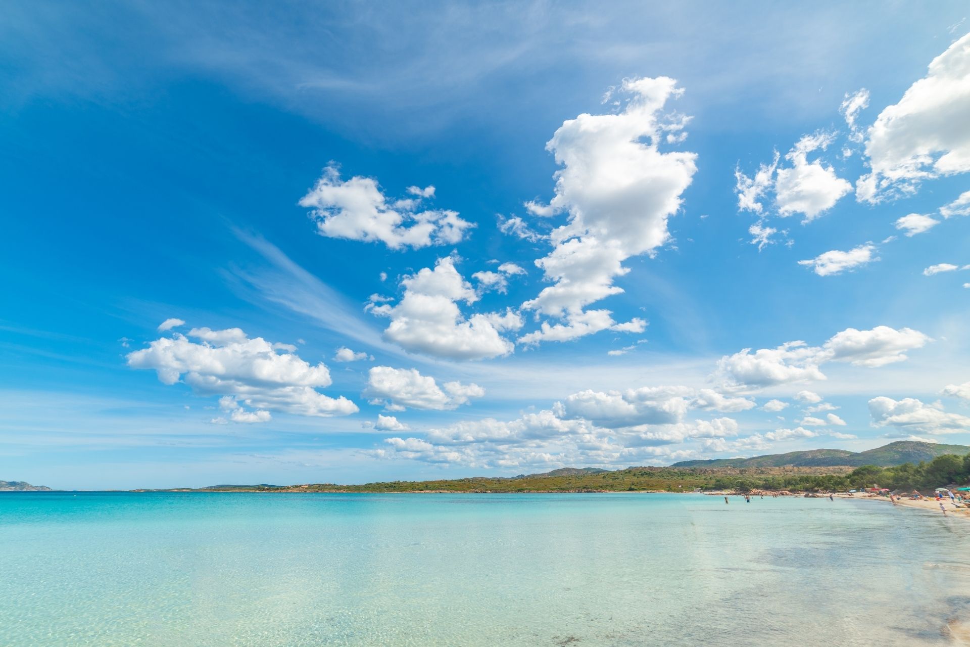View of a beach with blue sea and blue sky with clouds, people on the sand.