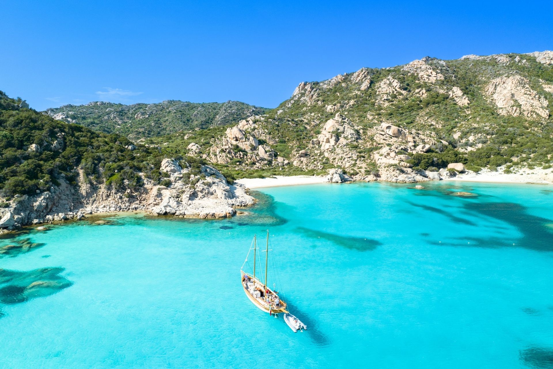 Image of a bathing area with a boat moored in crystal clear waters and a verdant rocky coast.