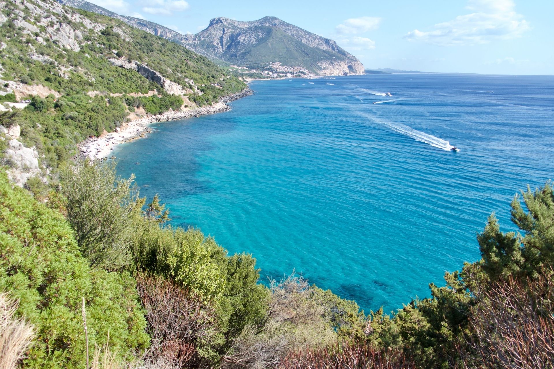 Panoramic view of a coastline with blue and green sea, with a moving bus in the background.