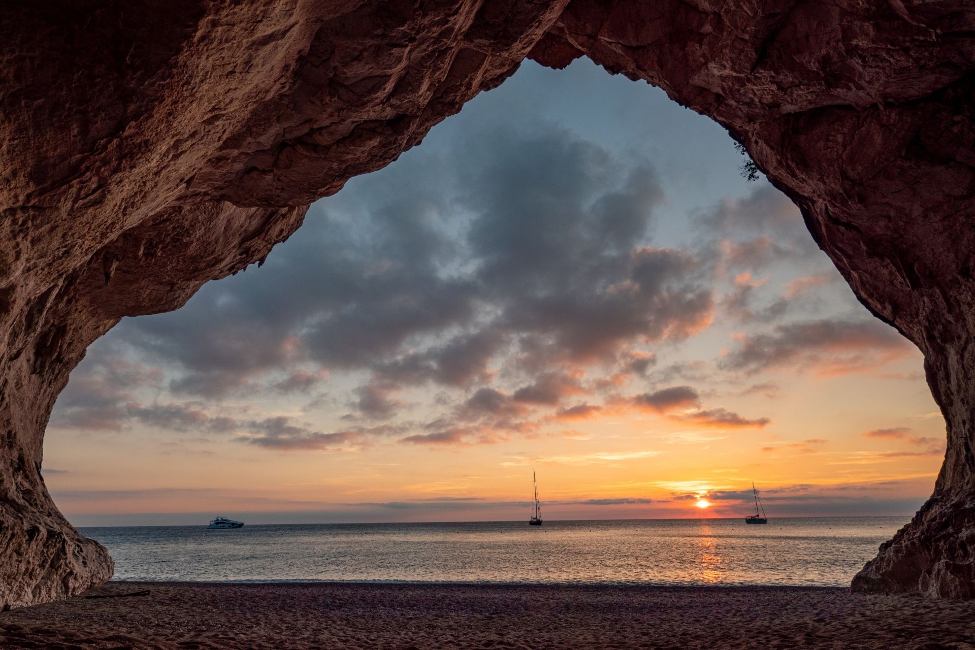 Panoramic view of a sea with sailing boats and sunset sky, from a natural cave.