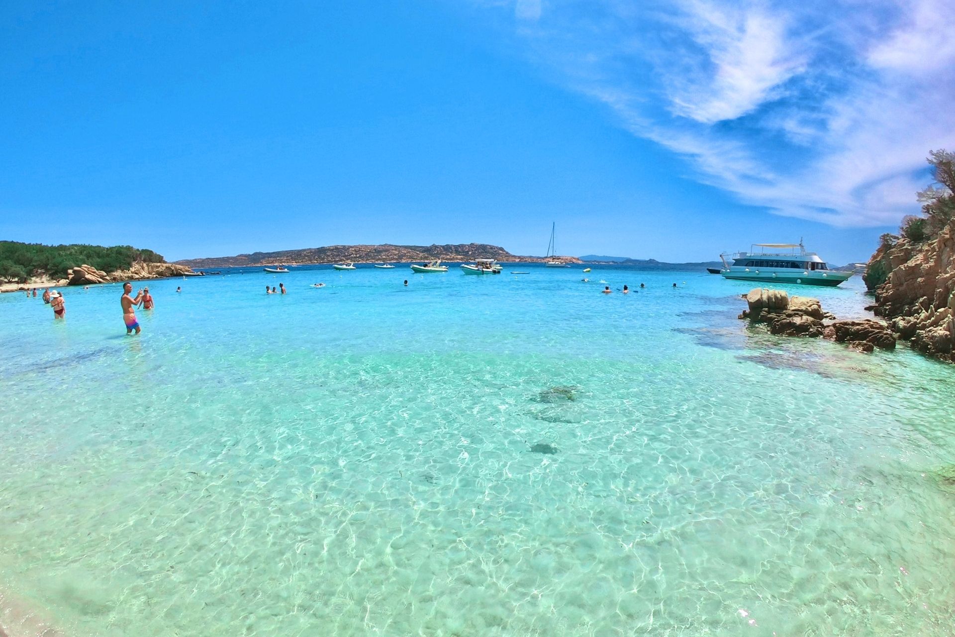 Immagine di un gruppo di persone che si divertono in acqua cristallina con barche e yacht in lontananza.