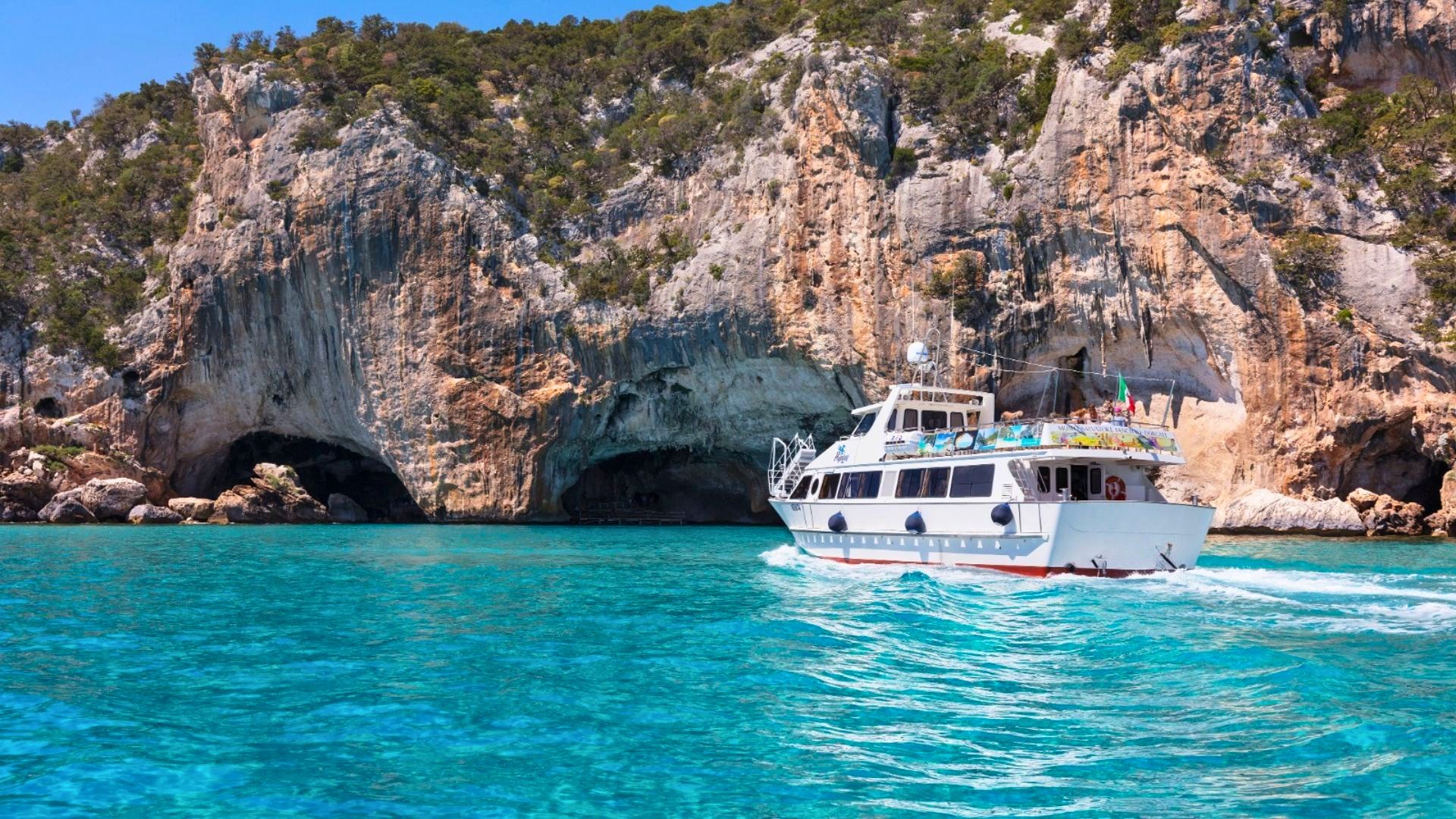 Ein Motorschiff segelt in einem Golf mit hohen Klippen und Höhlen