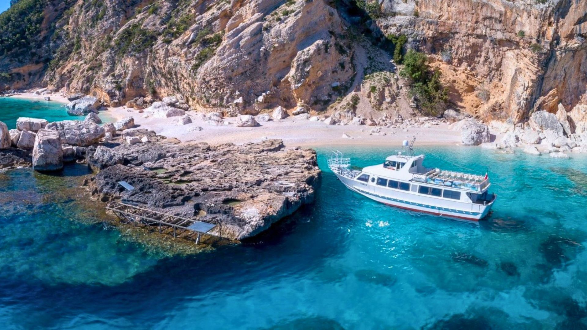 Bild eines Motorschiffs, das in einer Bucht mit Klippen und weißem Sandstrand vor Anker liegt