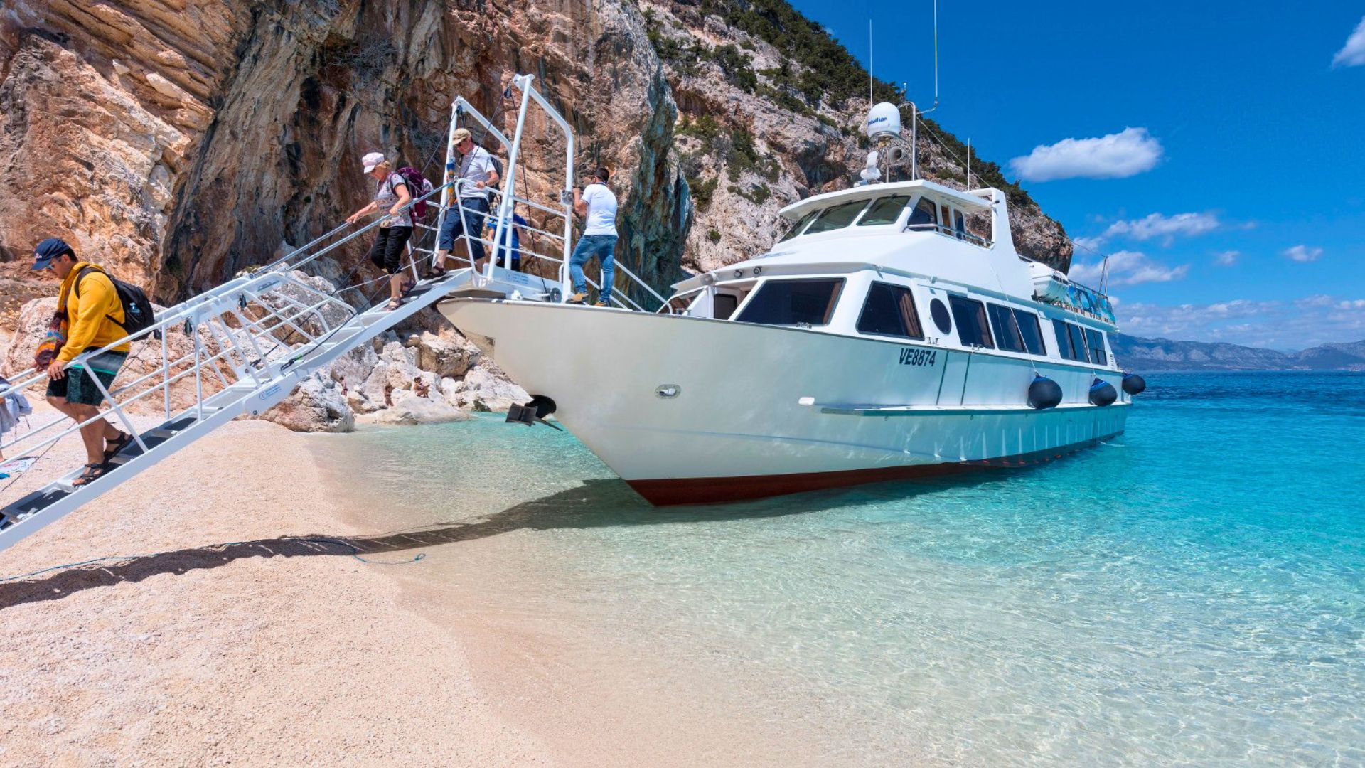 Menschen, die ein Motorschiff besteigen, das an einem Strand mit weißem Sand und kristallklarem Wasser festgemacht ist