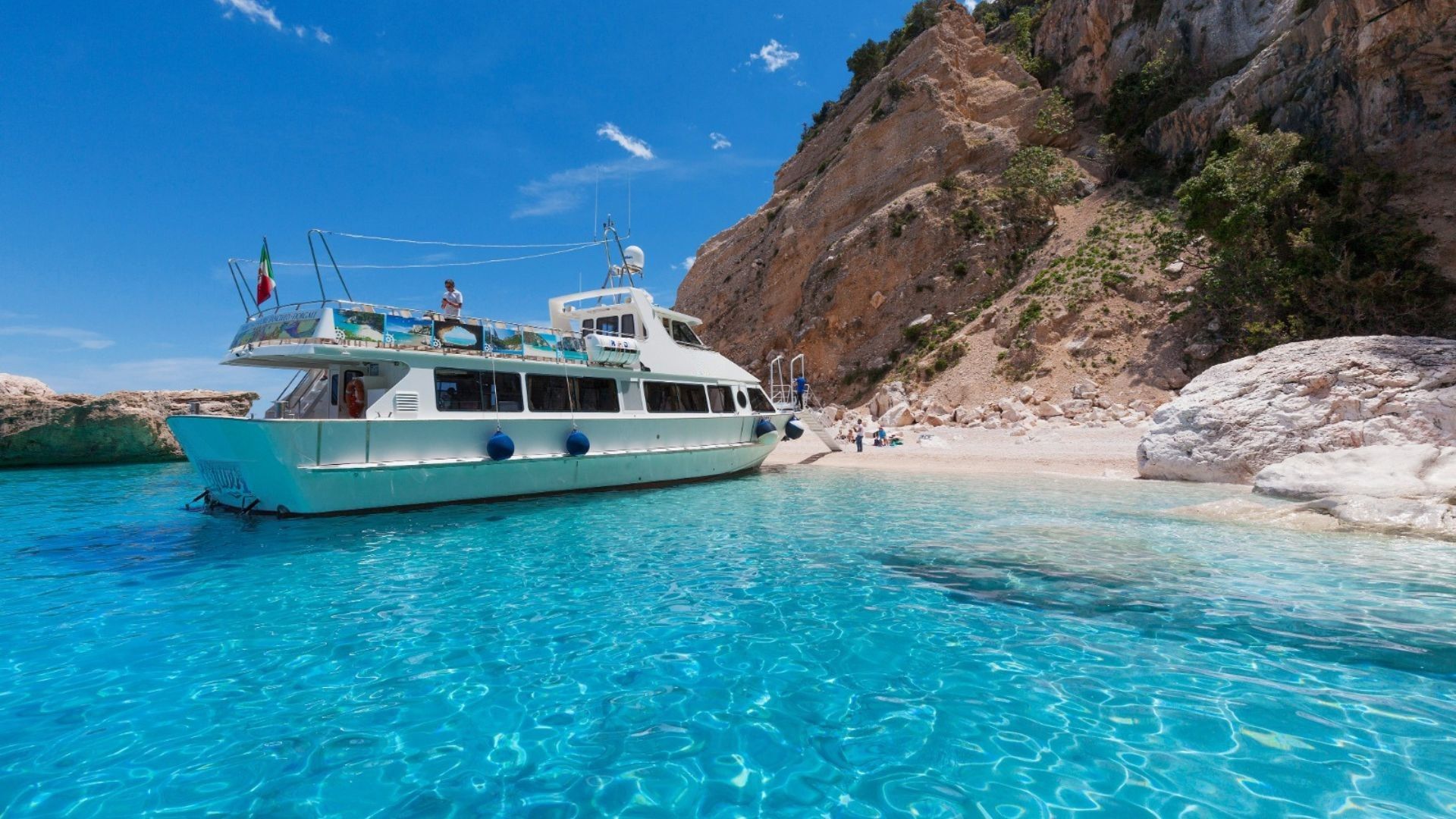 Ein Motorschiff segelt in kristallklarem Wasser vor einer Küste mit hohen Klippen und Klippen