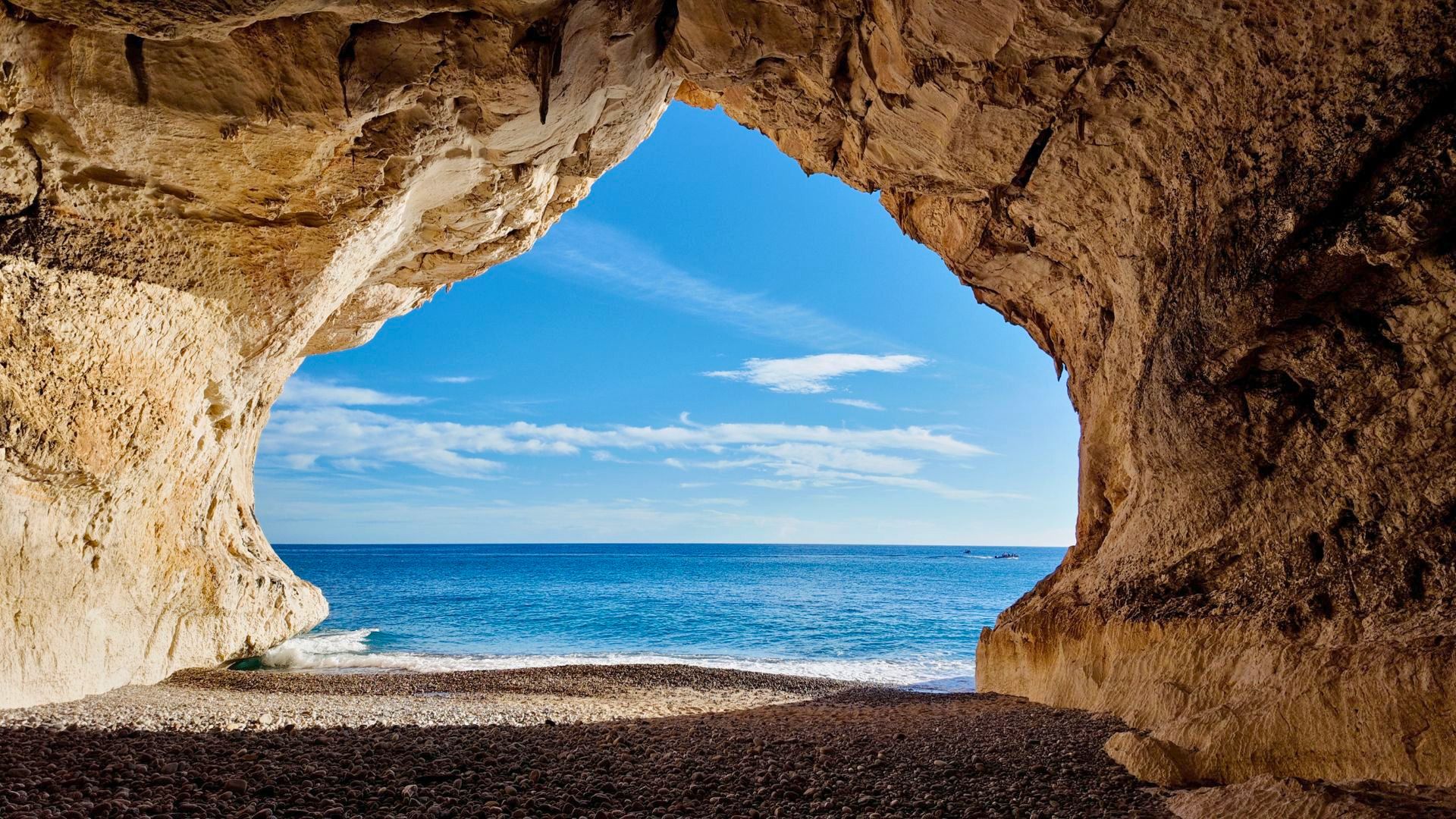 Ein Motorschiff segelt in einem Golf mit hohen Klippen und Buchten, mit einem Strand und einer sichtbaren Höhle
