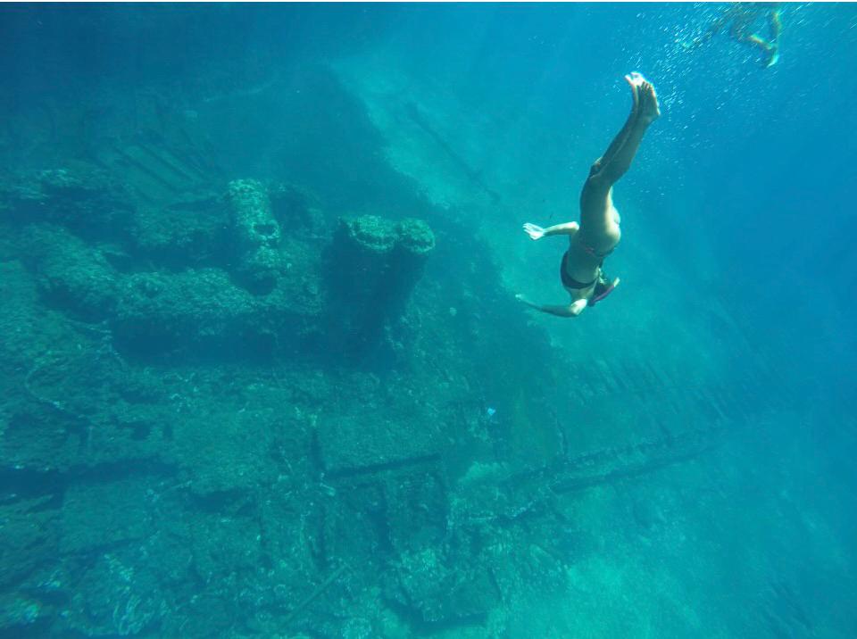 Una persona nada cerca de una costa salvaje y fascinante, con impresionantes acantilados, cuevas naturales y playas accesibles solo desde el mar.