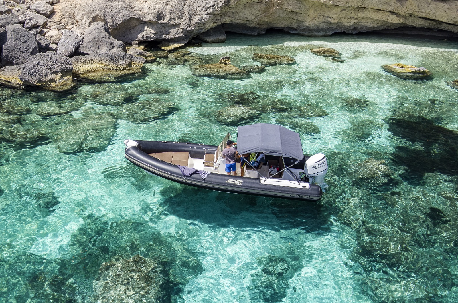 Imagen de una lancha en aguas cristalinas, cerca de acantilados y rocas, con personas a bordo disfrutando del espectacular paisaje.