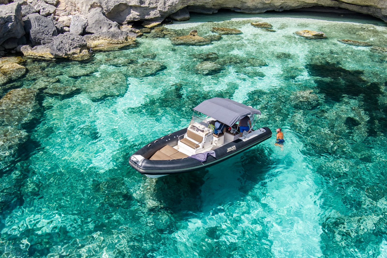 Imagen de una lancha con techo gris navegando en aguas cristalinas con rocas y acantilados a los lados.