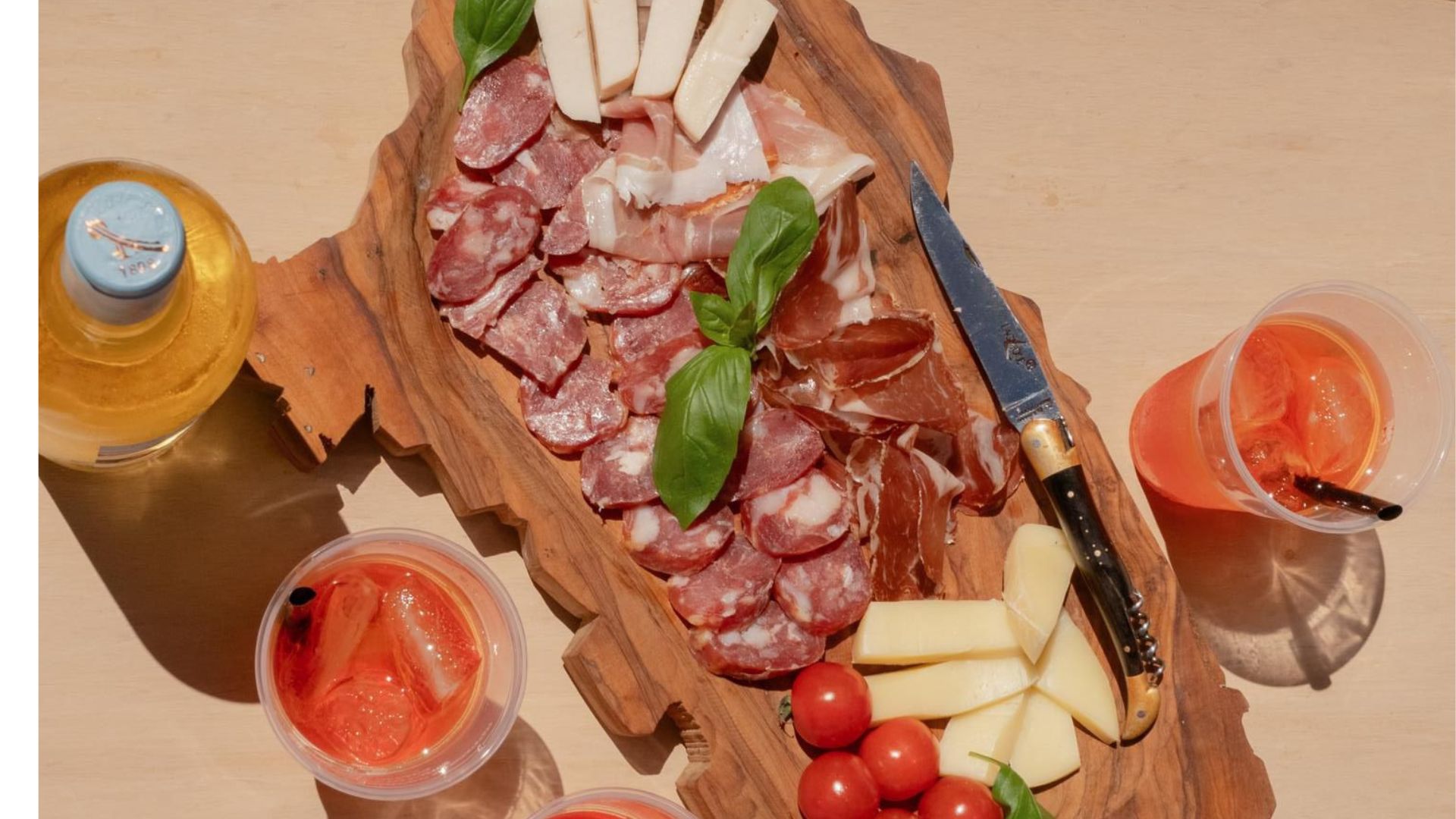 Picture of a cutting board with cold cuts, cheeses, vegetables and drinks
