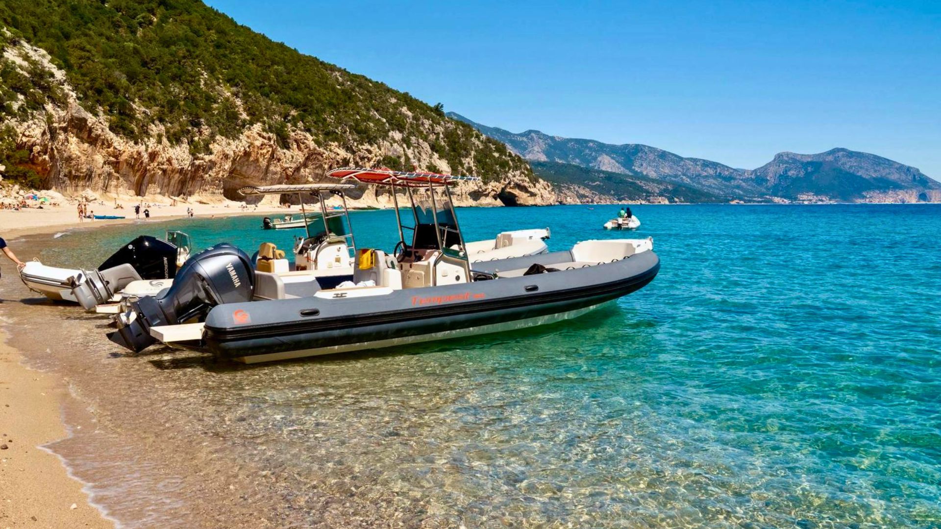 Two rafts parked on the beach of a rocky coast with crystal clear sea and mountains in the background. A boat tour experience in the Gulf of Orosei with an aperitif