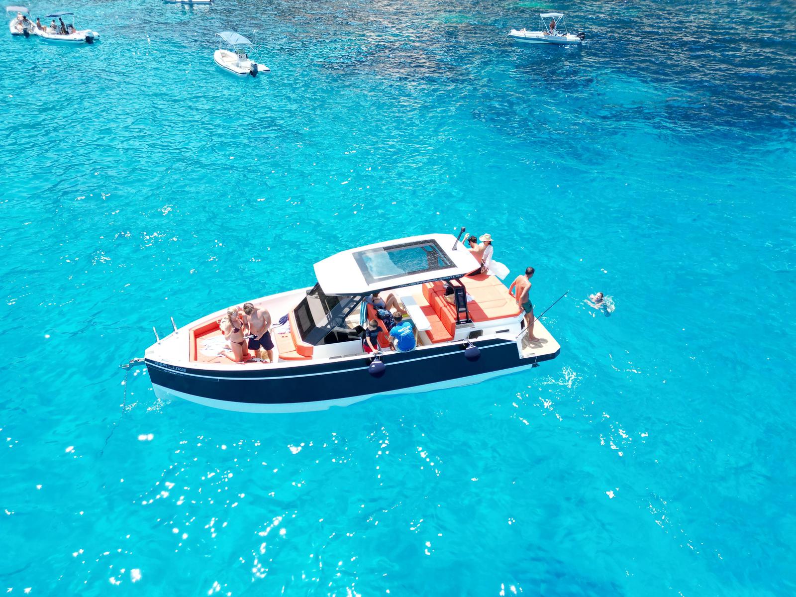 Mini yacht with people on board and one person diving into the blue, transparent water.