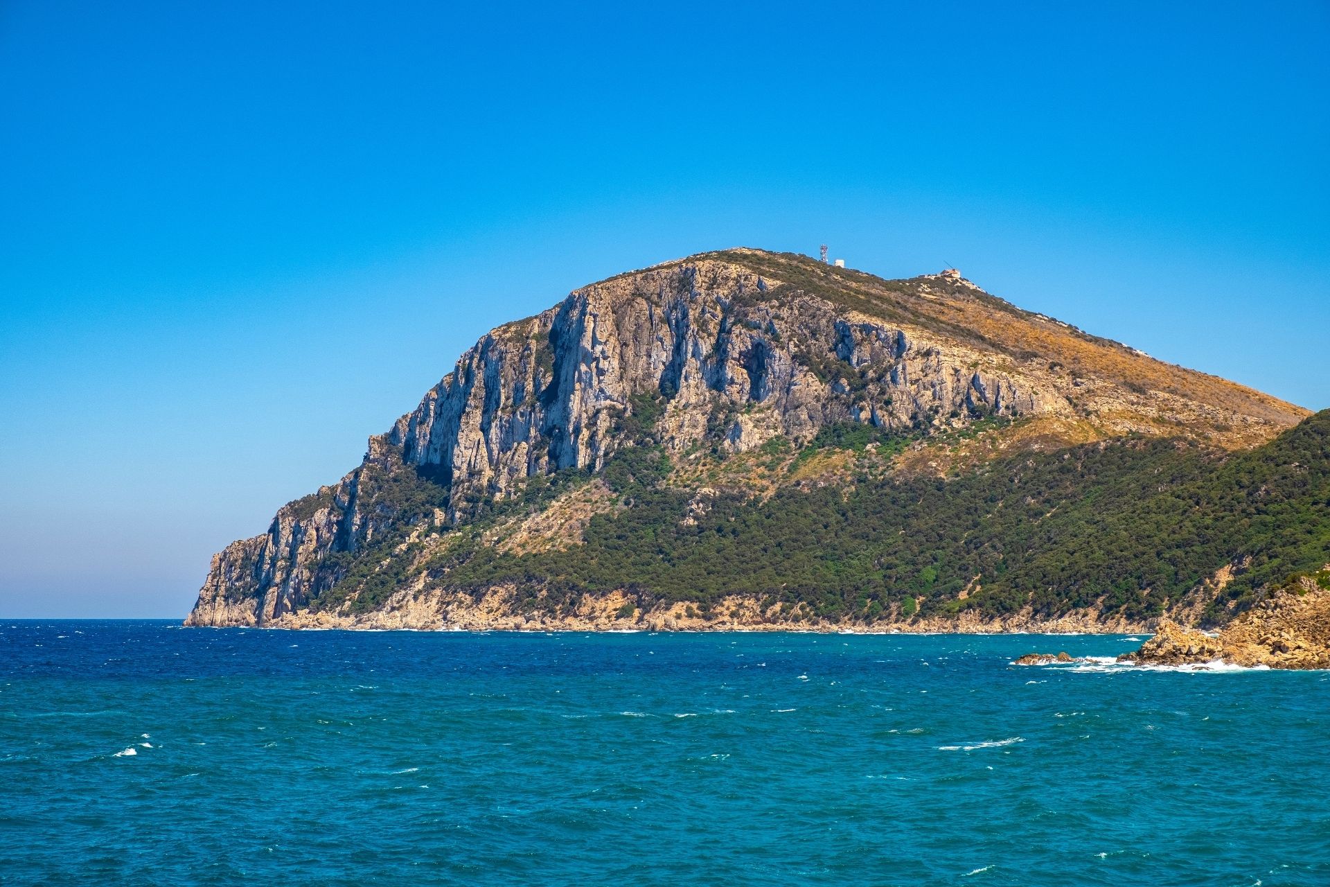 Montagne côtière avec des collines verdoyantes et une mer bleue sous un ciel bleu.