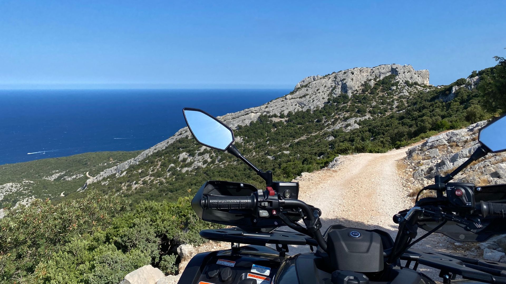 Un quad si trova su un sentiero sterrato che conduce a una vista panoramica sul mare e sulle montagne