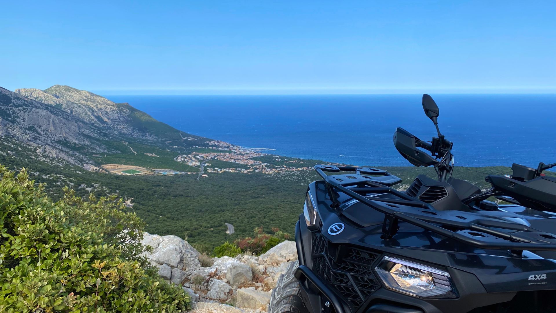 Un quad parcheggiato su un sentiero di montagna con vista sul mare e sulla costa sarda