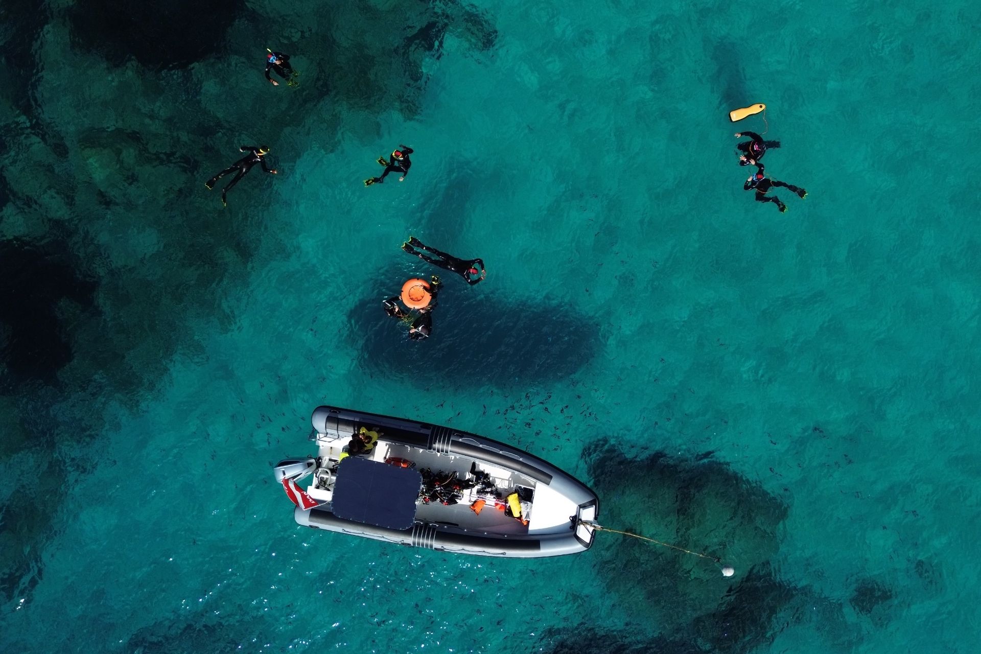 Imagen de un grupo de personas haciendo snorkel en el Área Marina Protegida de Tavolara, en el noreste de Cerdeña. Puedes ver aguas cristalinas, peces y corales y un bote amarrado.
