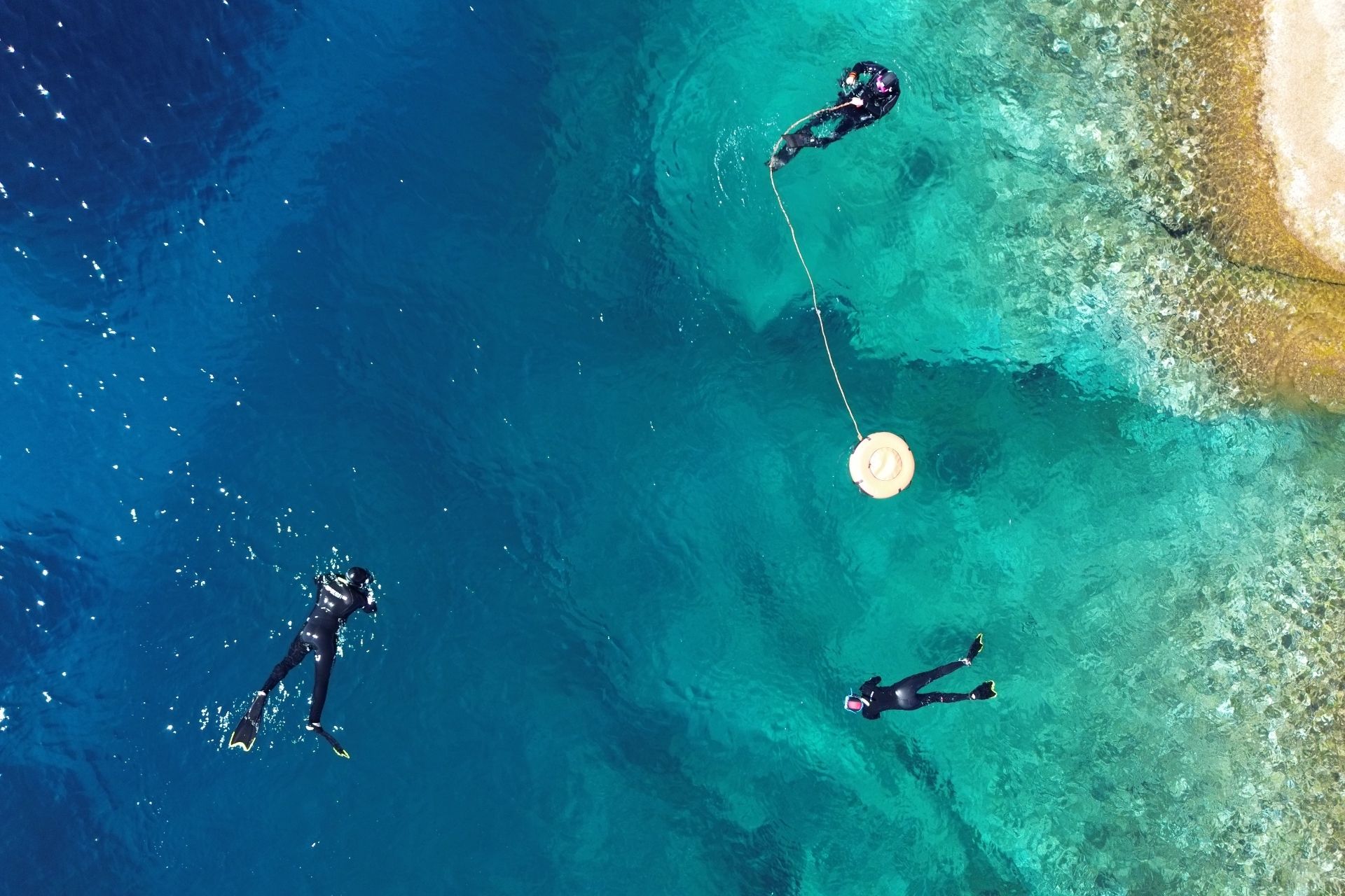 Tres personas bucean con equipo de buceo, conectadas por una cuerda, en aguas cristalinas.