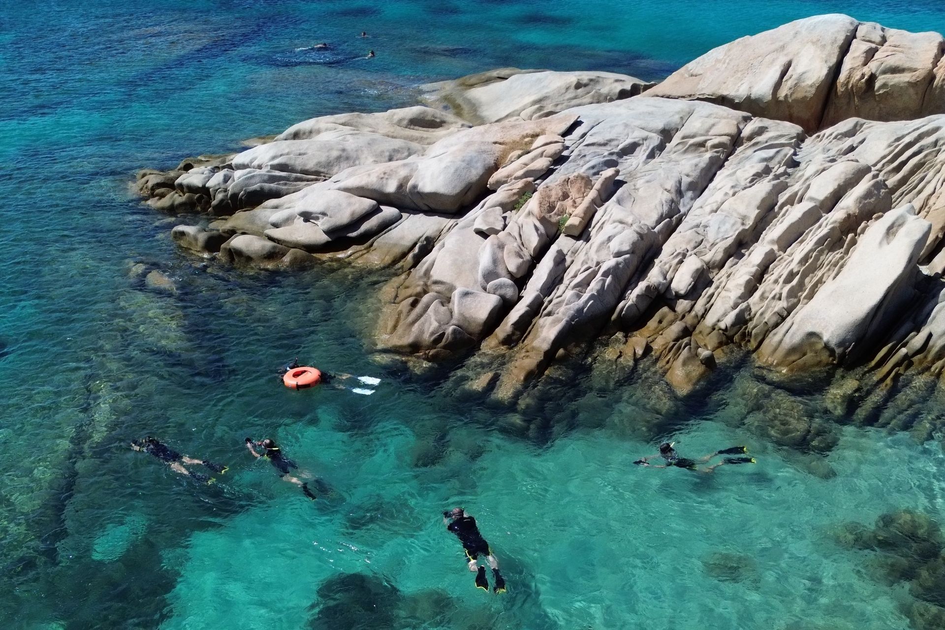 Gente buceando en aguas cristalinas con rocas de fondo