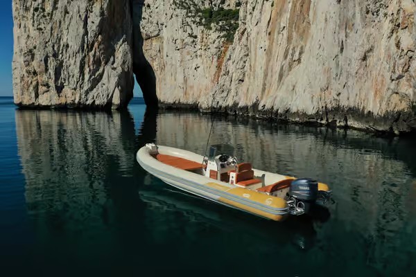 Immagine di un gommone ormeggiato vicino ad una scogliera con acque cristalline e riflessi di luce.