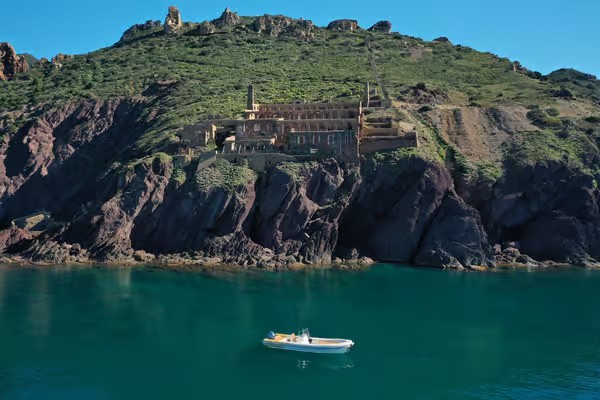 Un gommone naviga lungo la costa sud-ovest della Sardegna, tra natura selvaggia, archeologia industriale e acque cristalline.