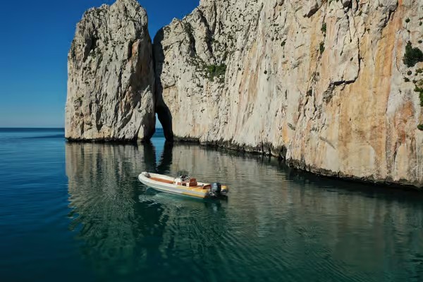 Immagine di un gommone che naviga tra le scogliere e le grotte marine della costa sud-ovest della Sardegna.