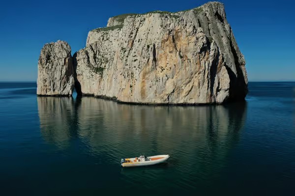 Immagine di un gommone che naviga in acque cristalline con una scogliera sullo sfondo.