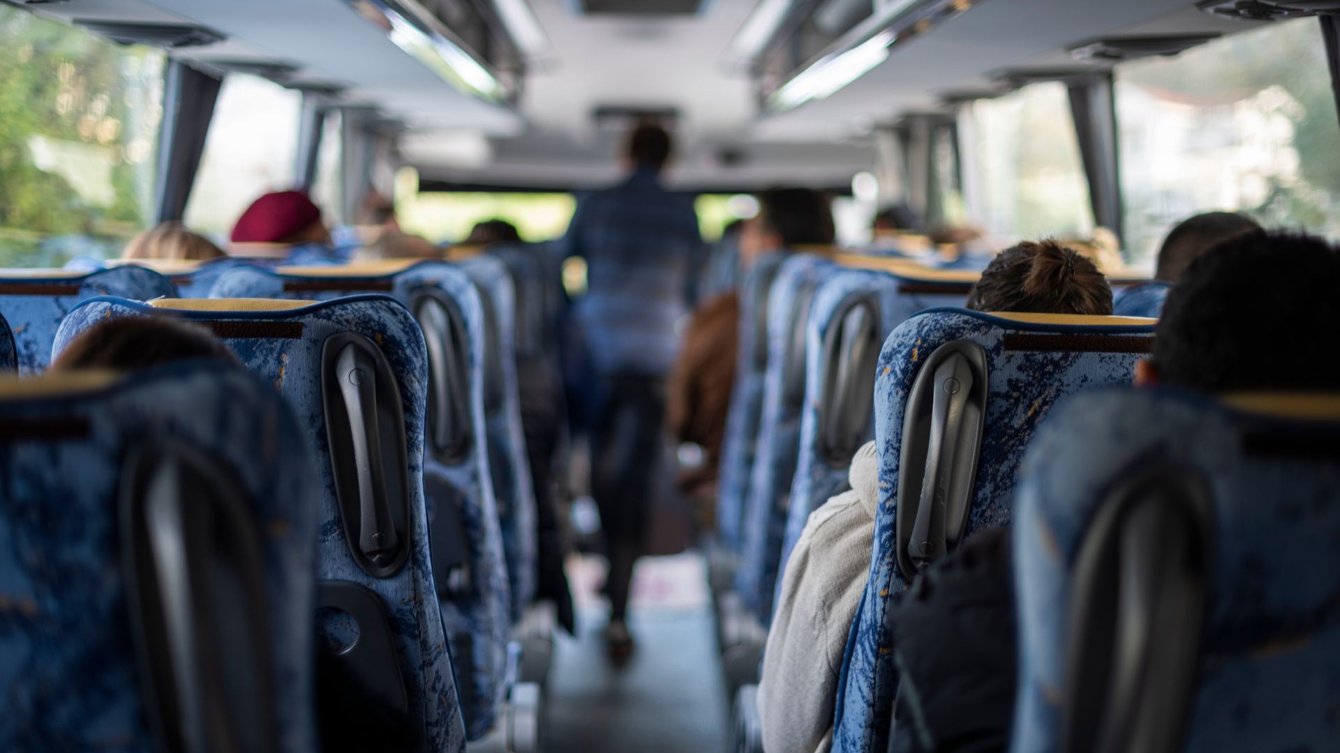 Immagine di un bus con passeggeri seduti e un uomo in piedi nell'ingresso del veicolo