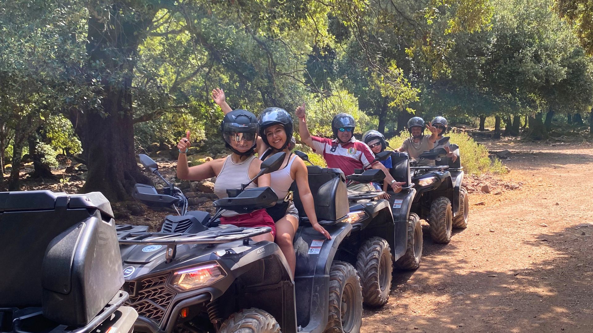 Un gruppo di persone in motoquad percorrono un sentiero sterrato tra boschi e montagne