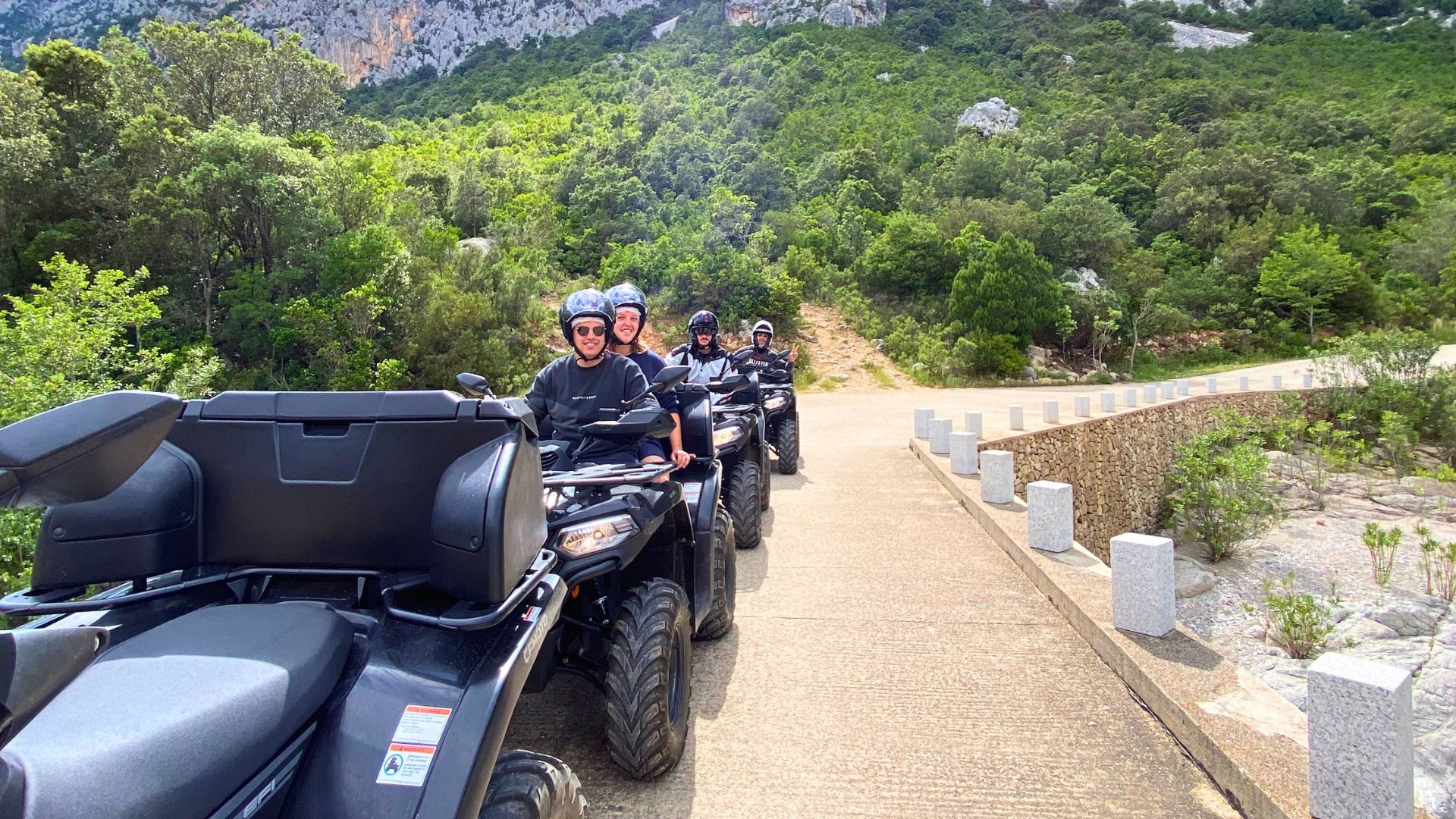 Persone in quad su un sentiero sterrato in una zona montuosa con vegetazione verdeggiante
