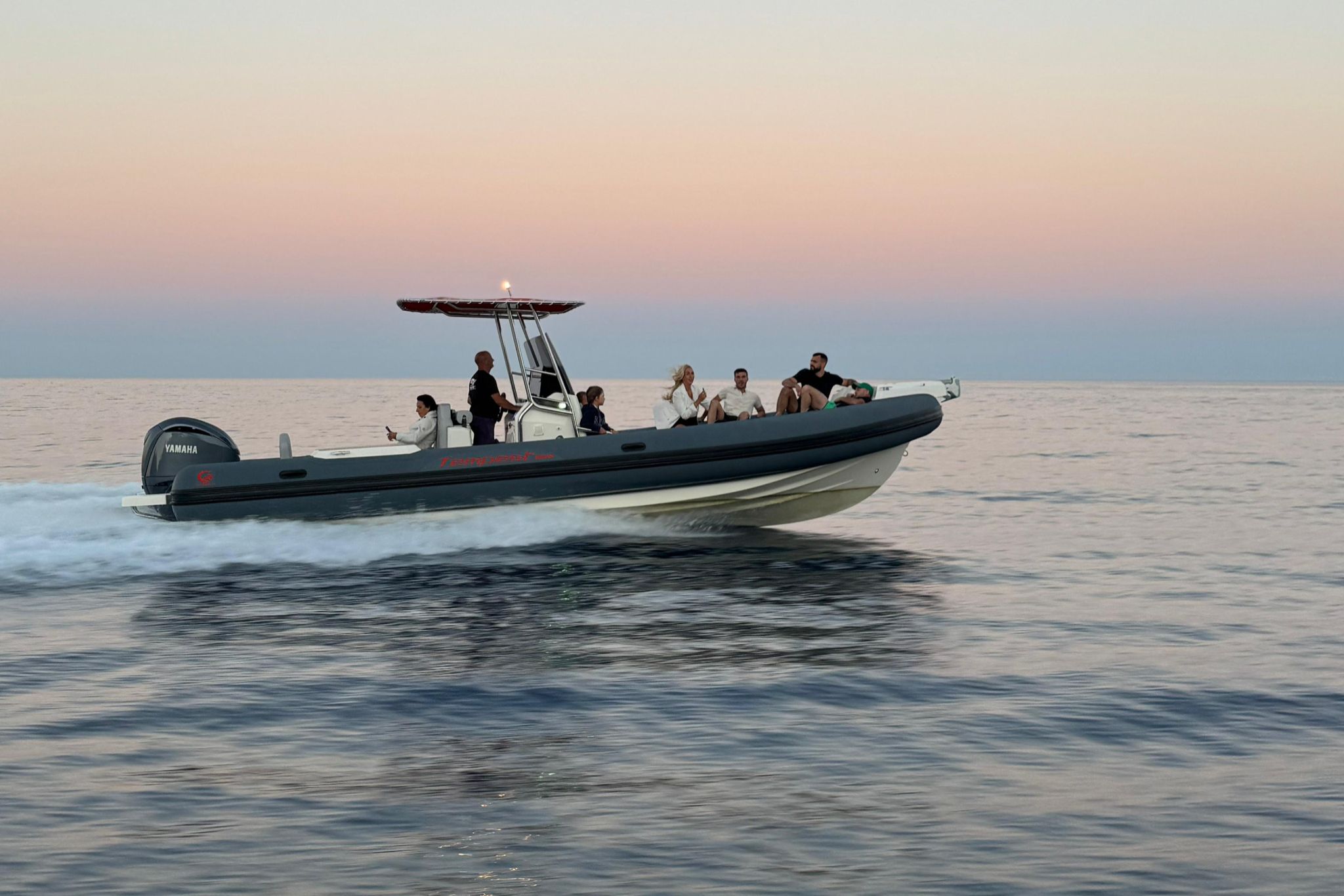 Group of people in a dinghy sailing on the sea at sunset