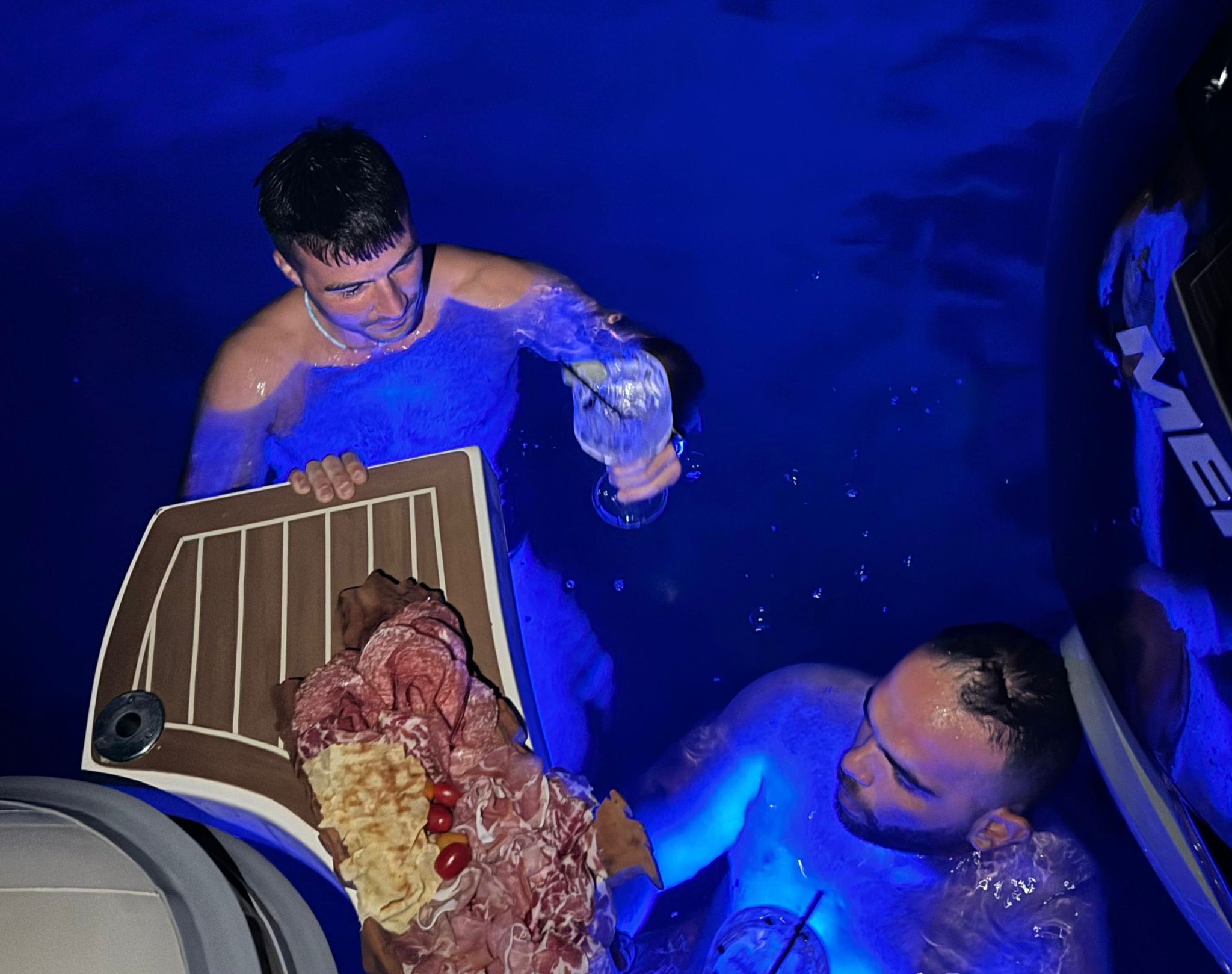 Two men in the water, one of whom holds a tray with food and drinks
