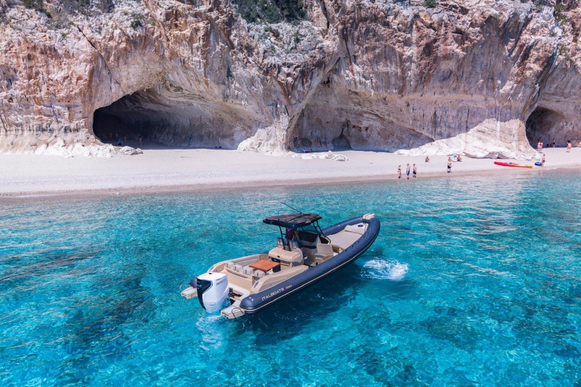 Image d'un dériveur naviguant dans des eaux cristallines avec des plages et des falaises en arrière-plan, idéale pour une visite touristique.