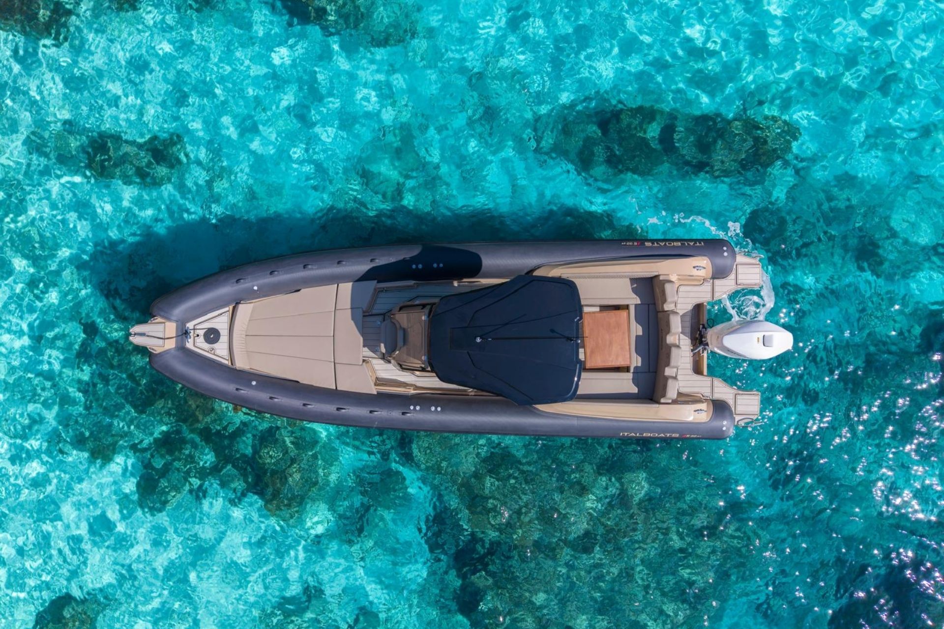 Image d'un dériveur naviguant dans des eaux cristallines avec des passagers dégustant un apéritif à bord. En arrière-plan, vous pouvez voir des falaises et de petites grottes.
