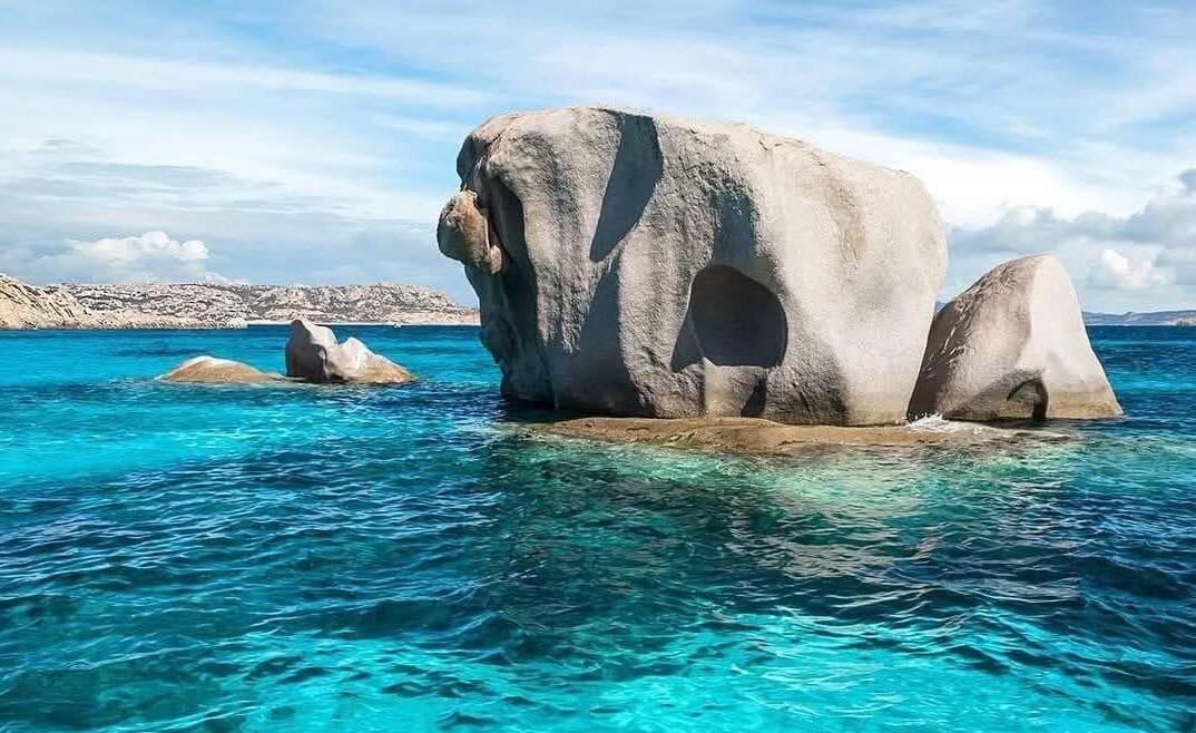 An image of an island with rocks and crystal clear water that could represent one of the stops of a speedboat tour in the Archipelago of La Maddalena.