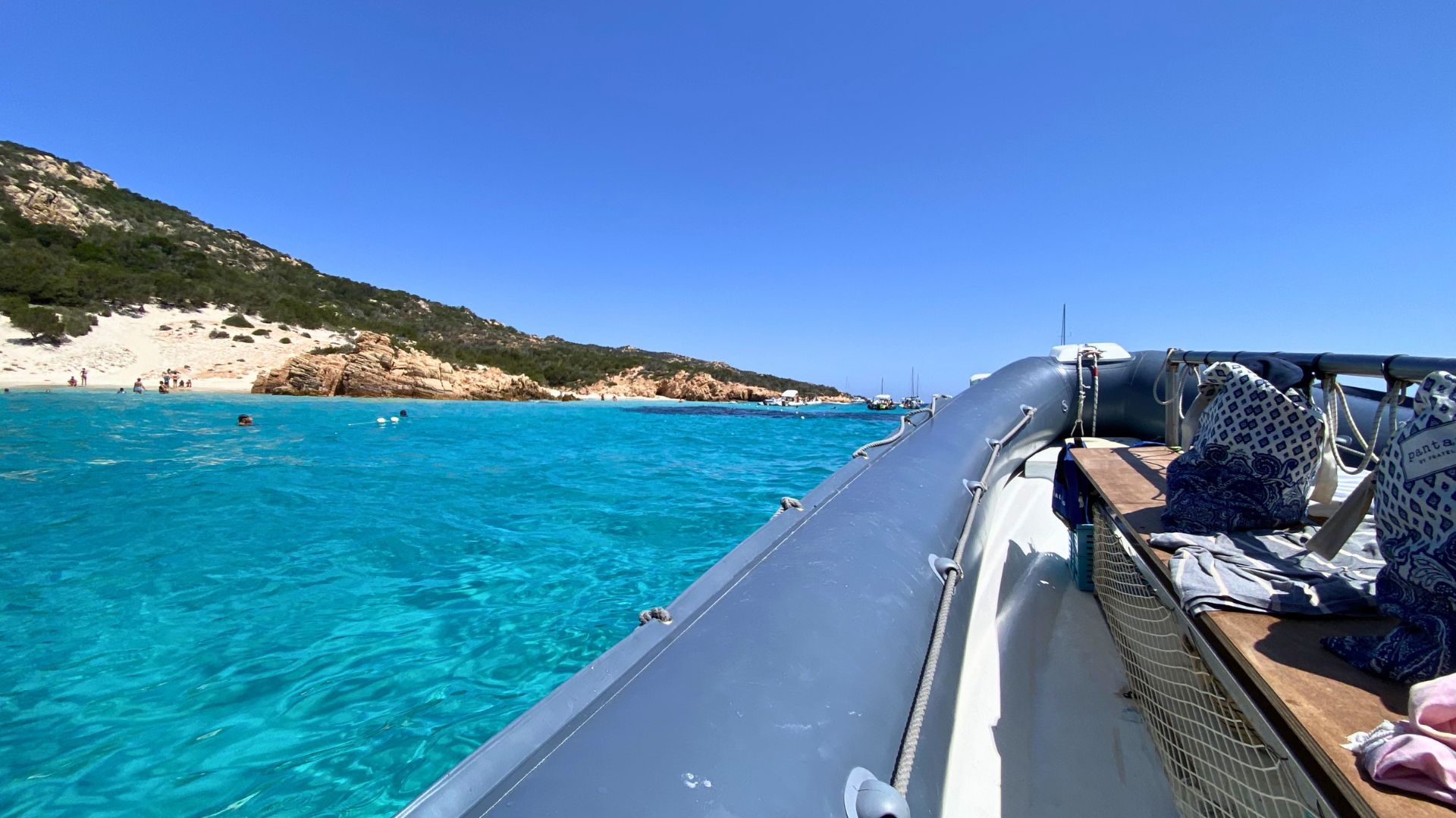 Un velero navega por aguas cristalinas con gente buceando cerca