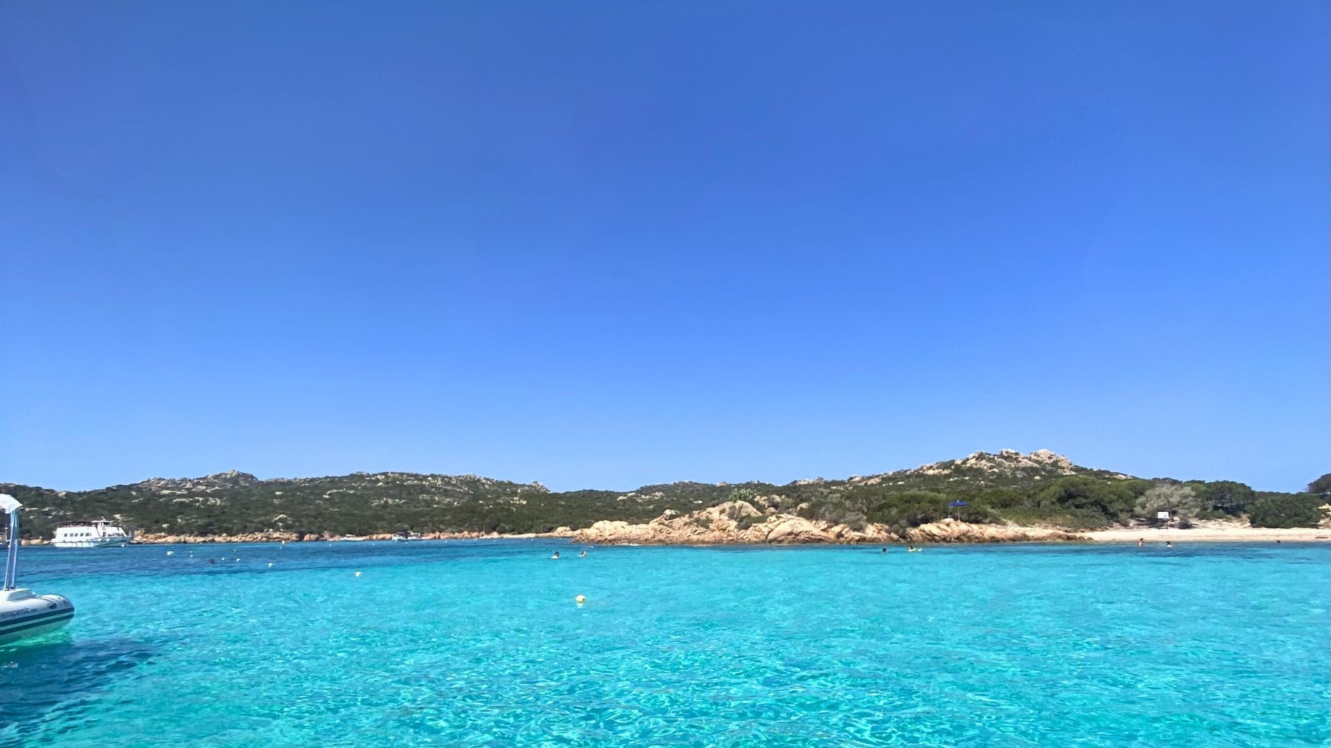 Imagen de una isla con mar cristalino y gente haciendo snorkel