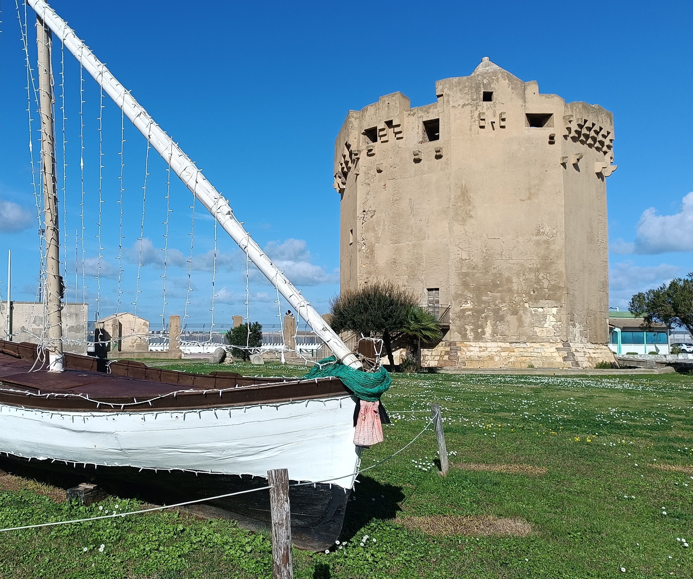 Una antigua torre de piedra junto a un barco amarrado en un parque verde con flores.