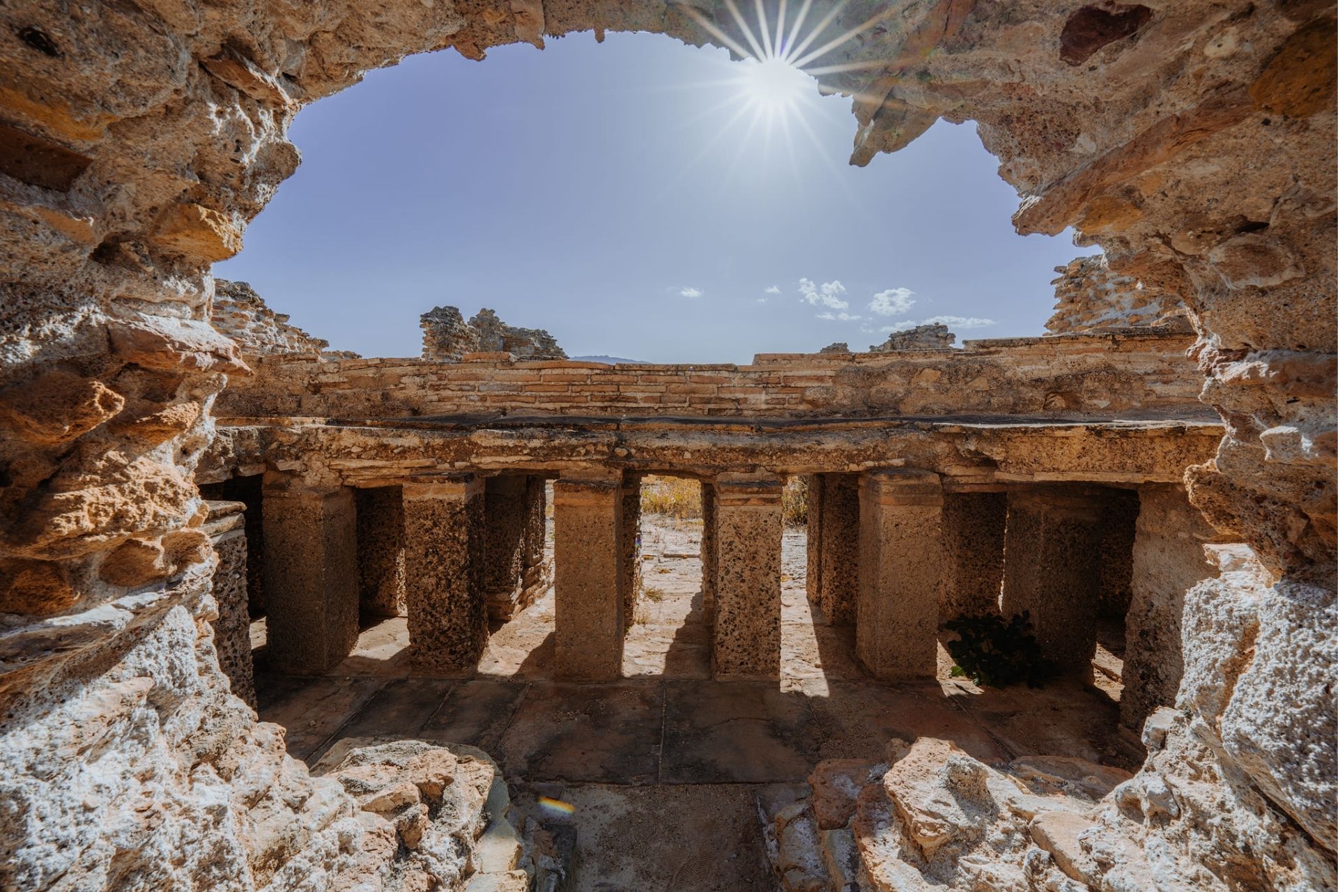Ruins of an ancient city seen from the sea with a kayak, under a bright blue sky.