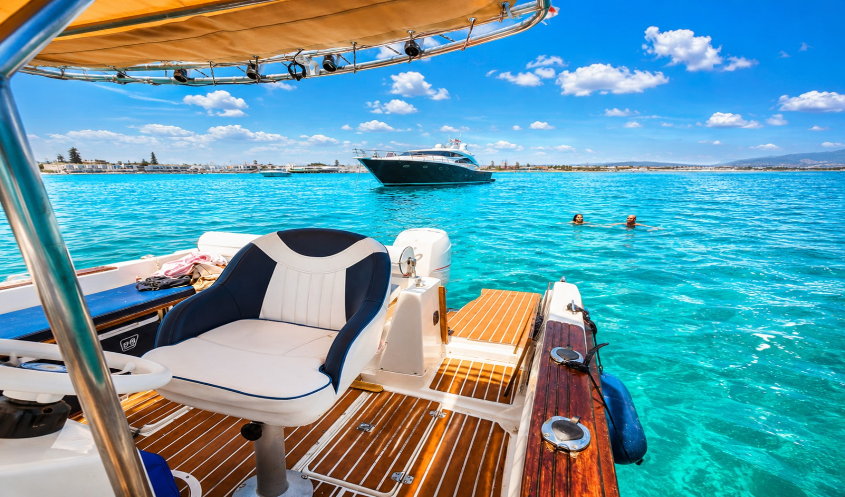 Image d'un bateau avec une personne nageant dans l'eau bleue, à l'arrière-plan un autre bateau et le paysage côtier.