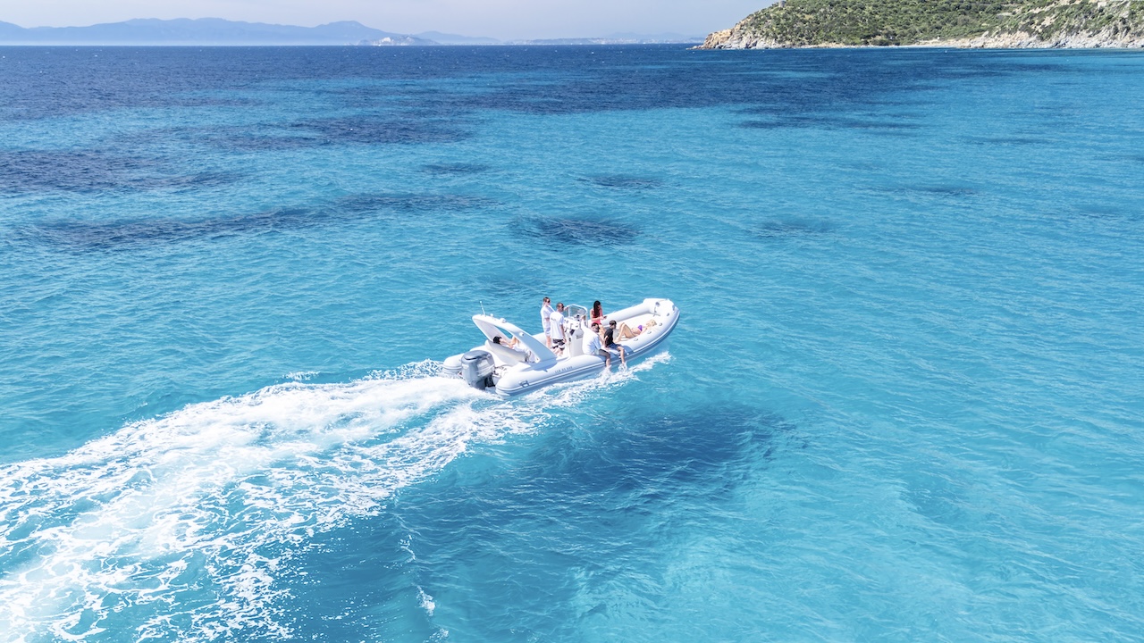 Un gruppo di persone in un gommone in acqua blu con una costa sullo sfondo