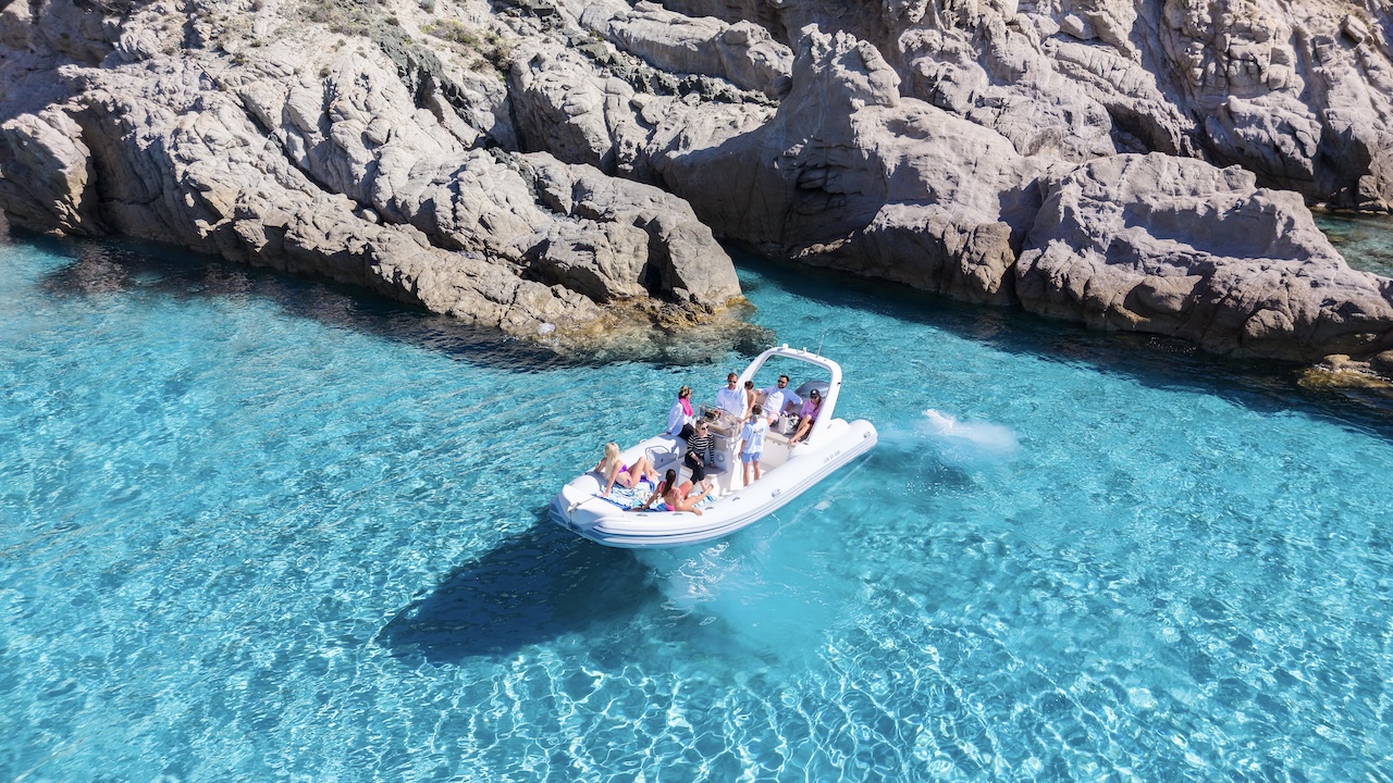 Un gruppo di persone su un gommone vicino alla costa con acque cristalline e rocce
