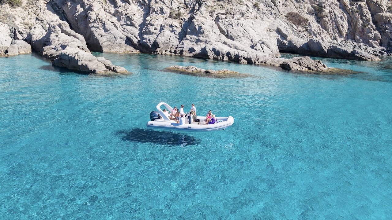 Un gruppo di persone in un gommone in acqua blu vicino a una costa rocciosa