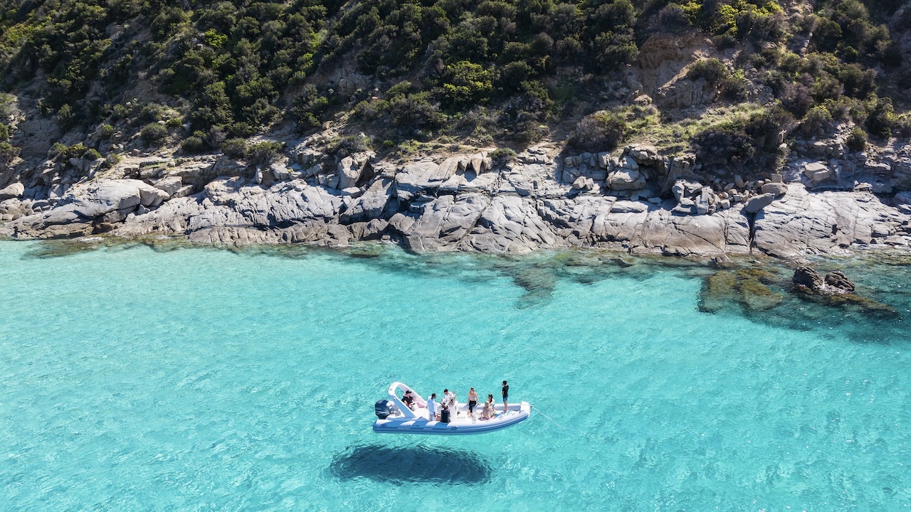 Un gruppo di persone su un gommone in acqua cristallina con uno sfondo roccioso
