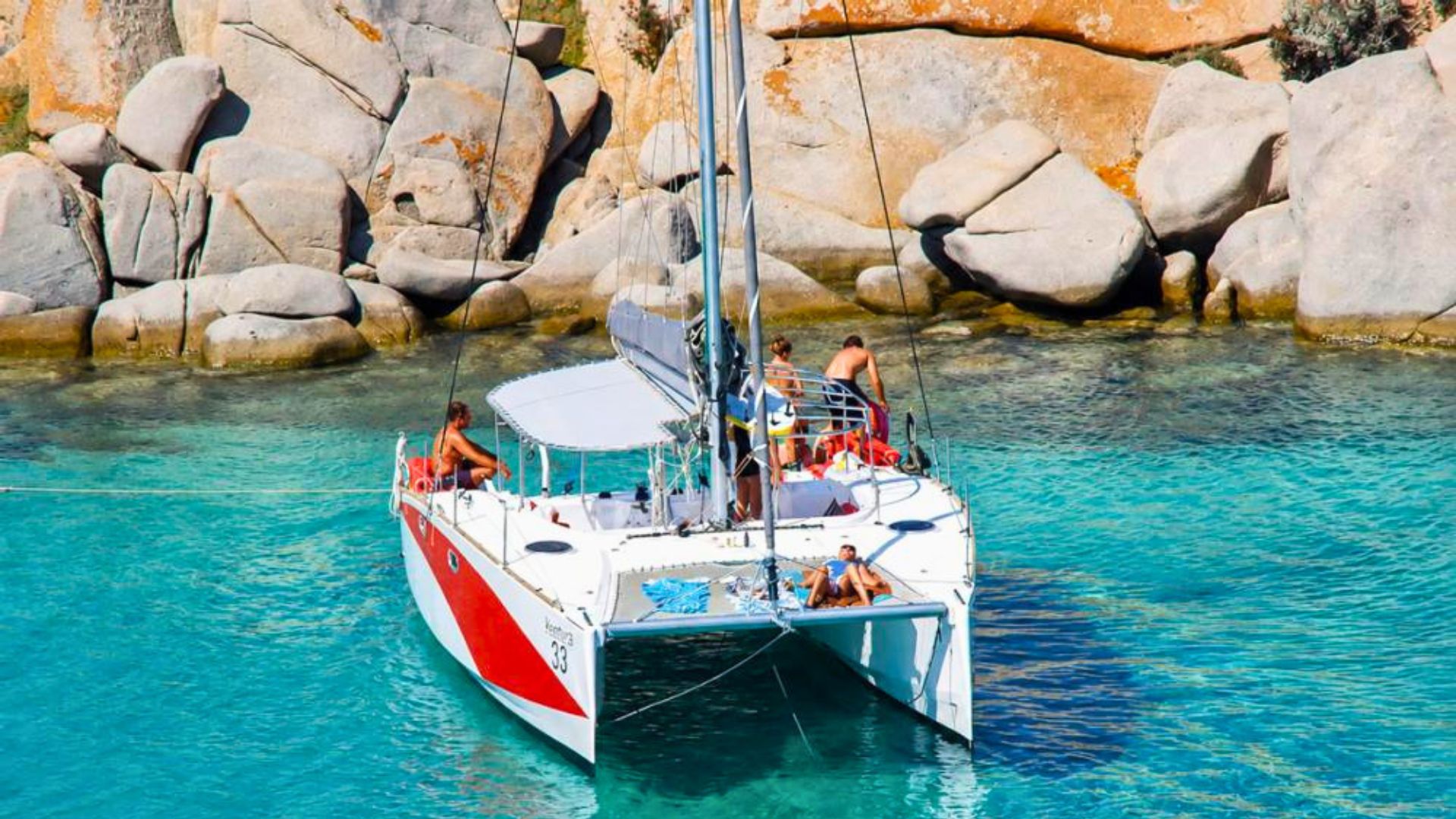 Catamaran à voile naviguant avec passagers à bord et falaises rocheuses en arrière-plan