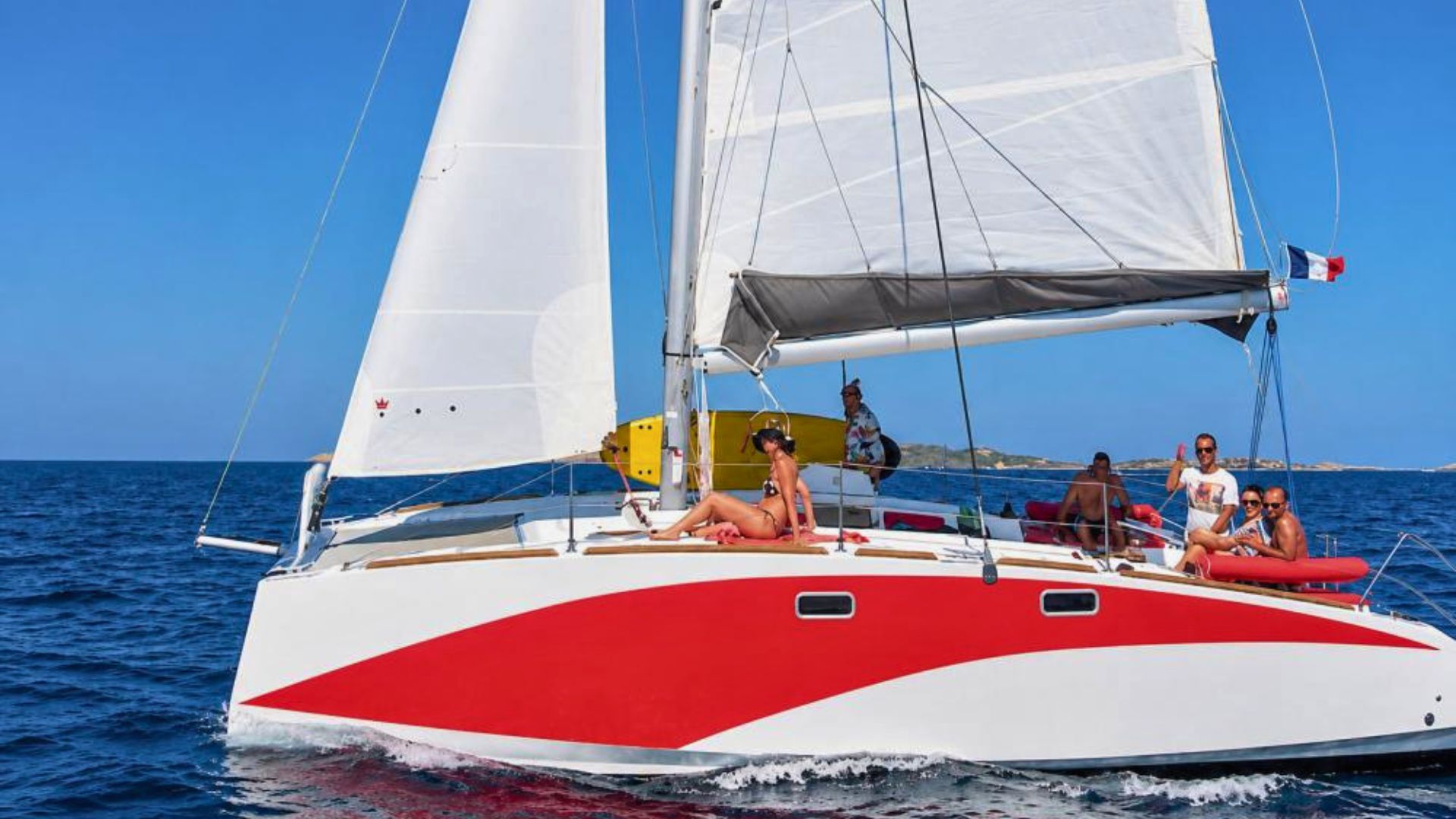 Groupe de personnes sur un catamaran à voile avec une mer calme et un ciel bleu, certains couchés et d'autres assis