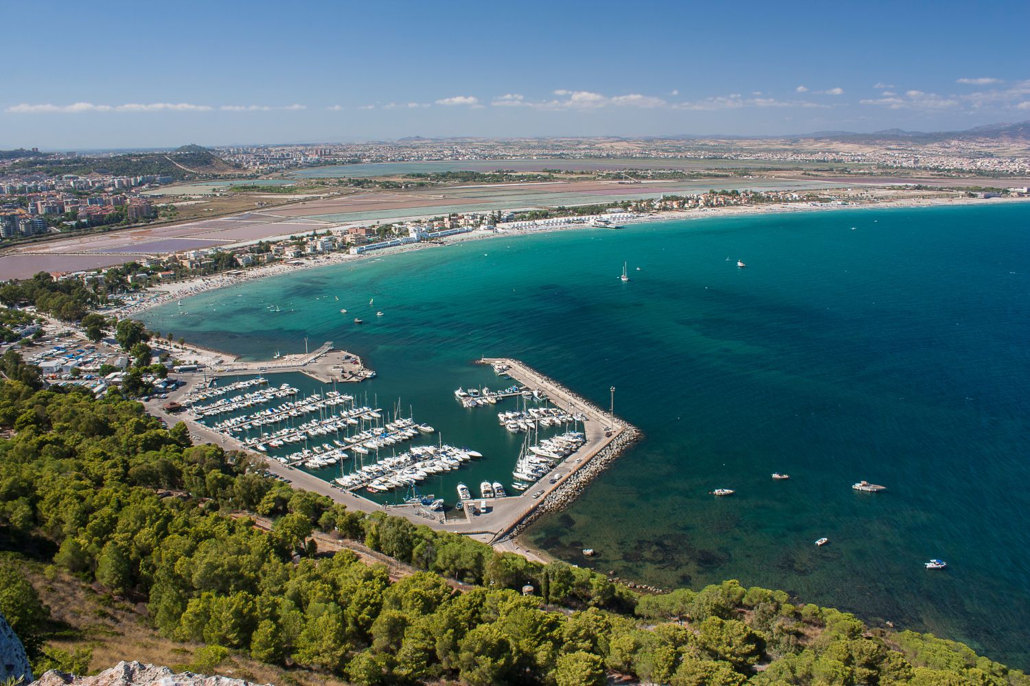 Vista aérea de una costa con un puerto y una playa, edificios y montañas al fondo