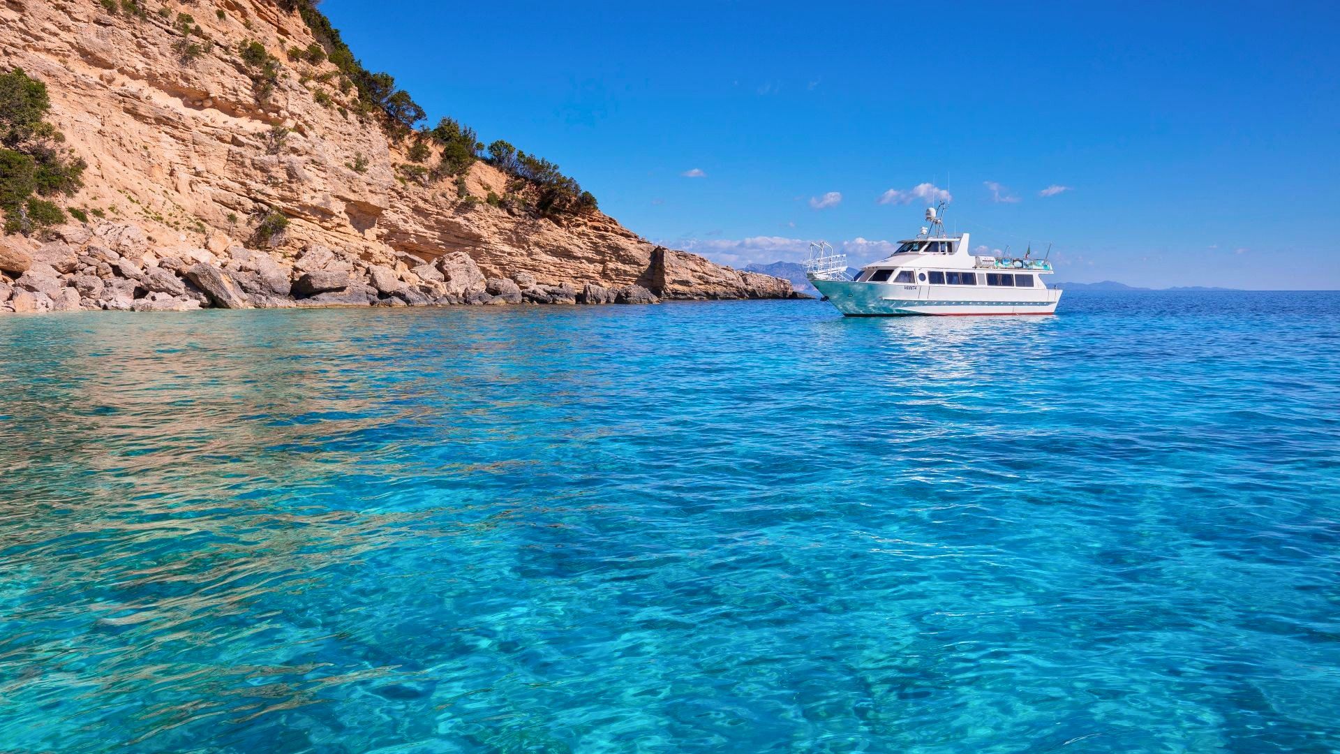 Ein Motorschiff segelt entlang einer Küste von außergewöhnlicher Schönheit, die sich durch hohe Klippen und kristallklares Wasser auszeichnet