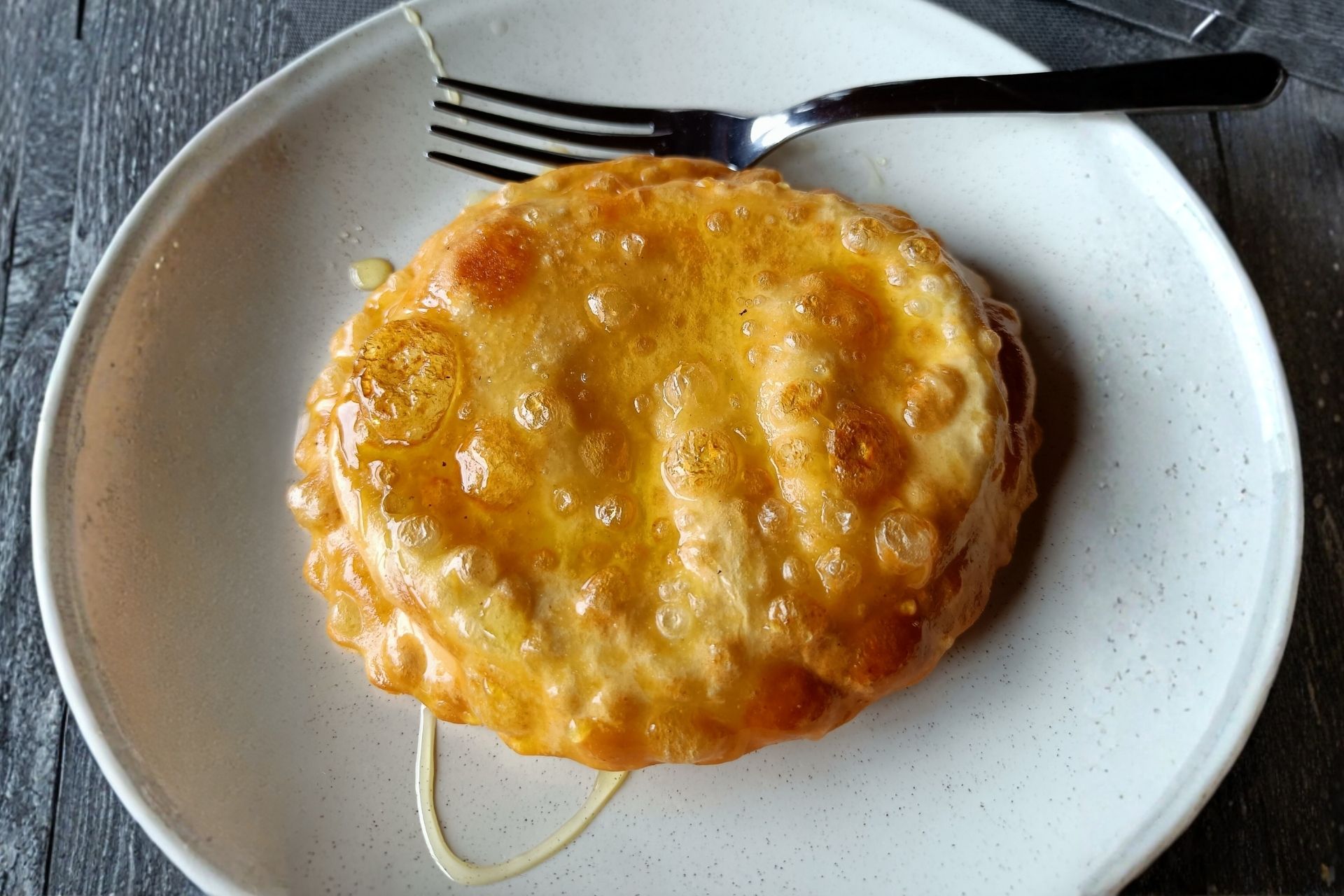 Eine Portion Seada, ein traditionelles sardisches Dessert, bedeckt mit Honig auf einem weißen Teller.