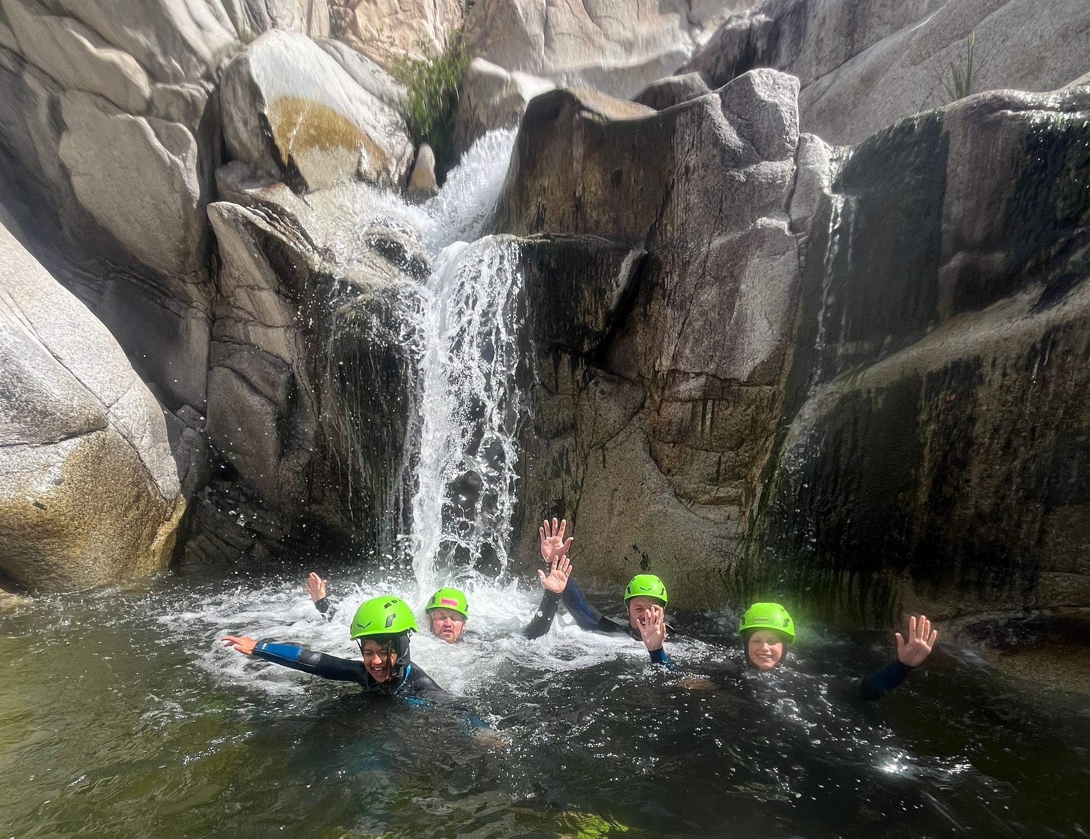 Gruppo di persone che si immergono in una cascata naturale con elmetti di protezione