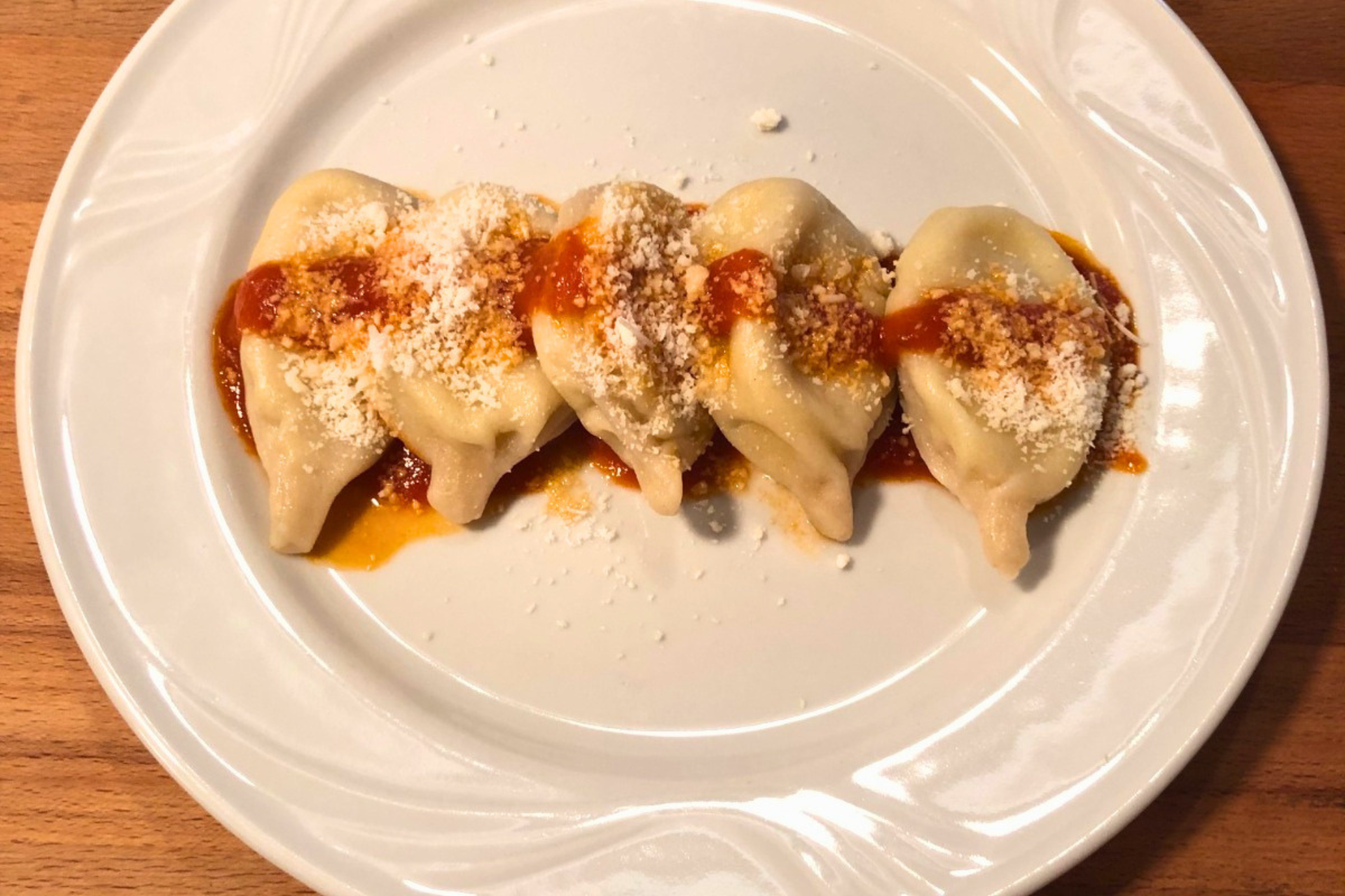 Une assiette de raviolis Tortoliesi ou de culurgiones sur une assiette blanche avec des garnitures et du fromage râpé
